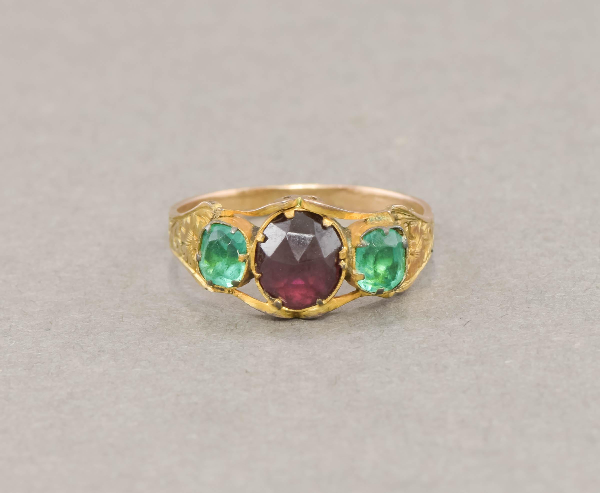 Wonderful color & glow combine with intricate floral engraving in this dainty antique garnet and paste ring. It is estimated to date to the 1850's.

Crafted of gold testing around 9K (with a bloomed/gilded finish), the ring features an elegant three