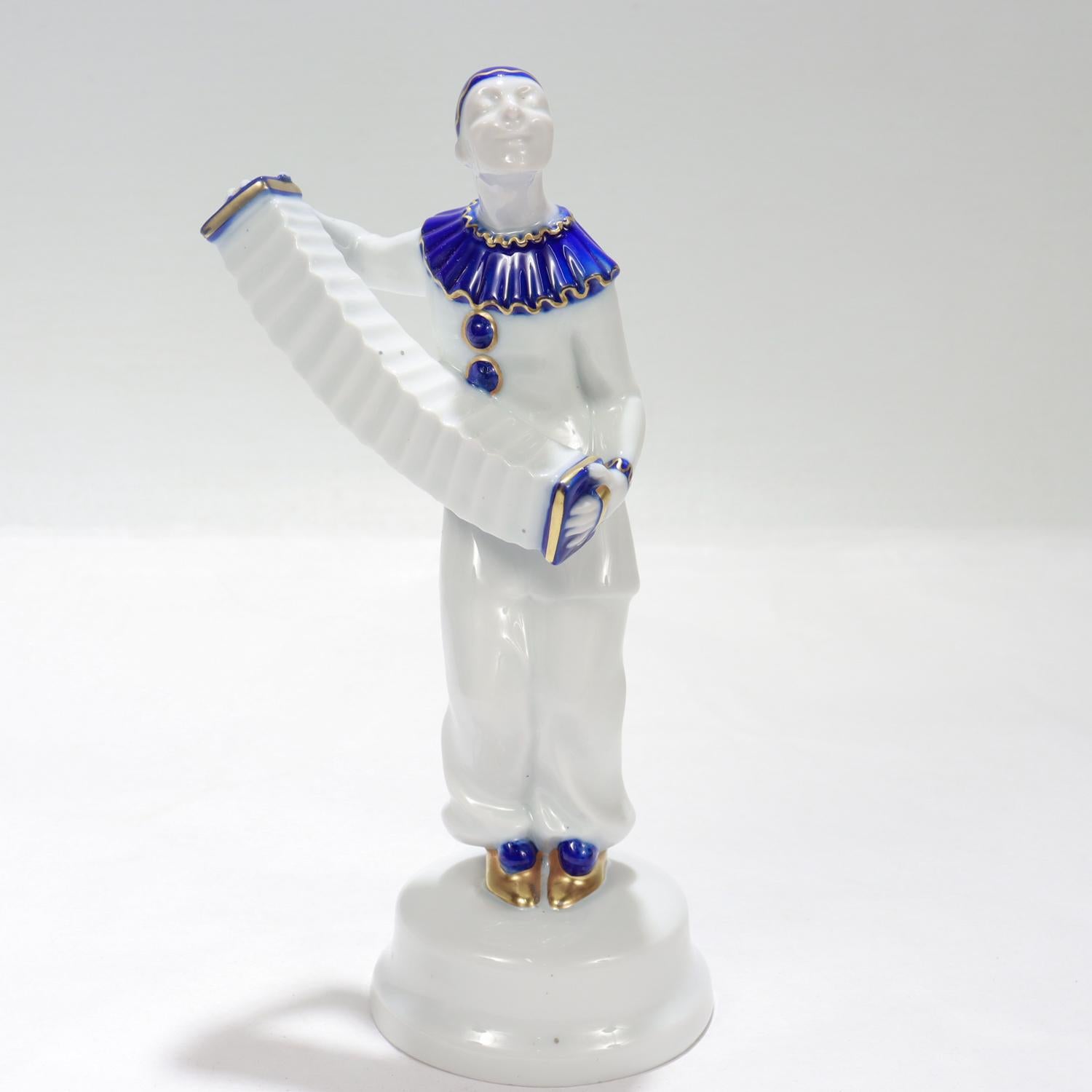 Una bella statuetta antica di porcellana tedesca Jugendstil.

Disegnata da Albert Caasmann per Rosenthal nel 1916.

A forma di clown Pierrot che suona una fisarmonica con accenti blu e dorati su un basamento.

La base è contrassegnata dal marchio