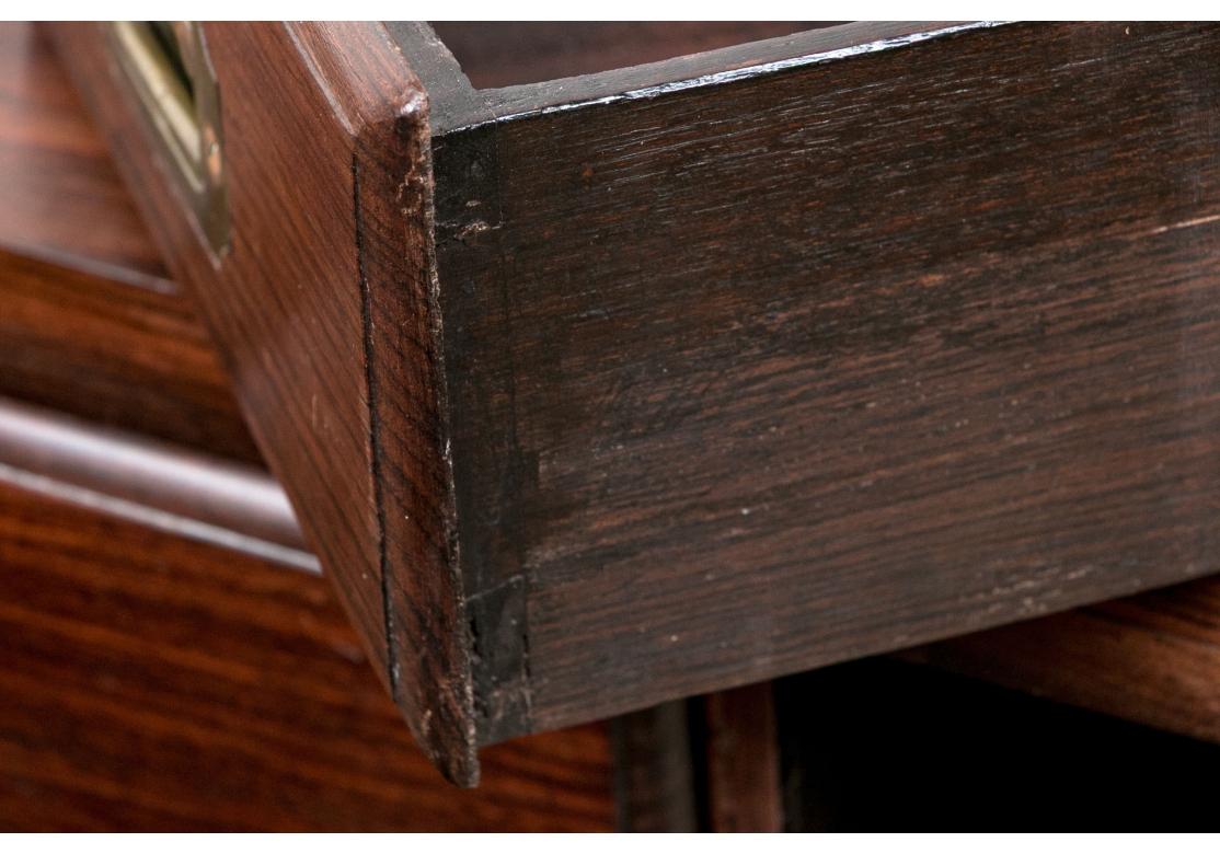 A finely constructed two part campaign chest with the classic brass banding overall and inset brass carry handles. The top chest has two short drawers flanking a center one that opens to a secretary with a replaced green felt writing surface,