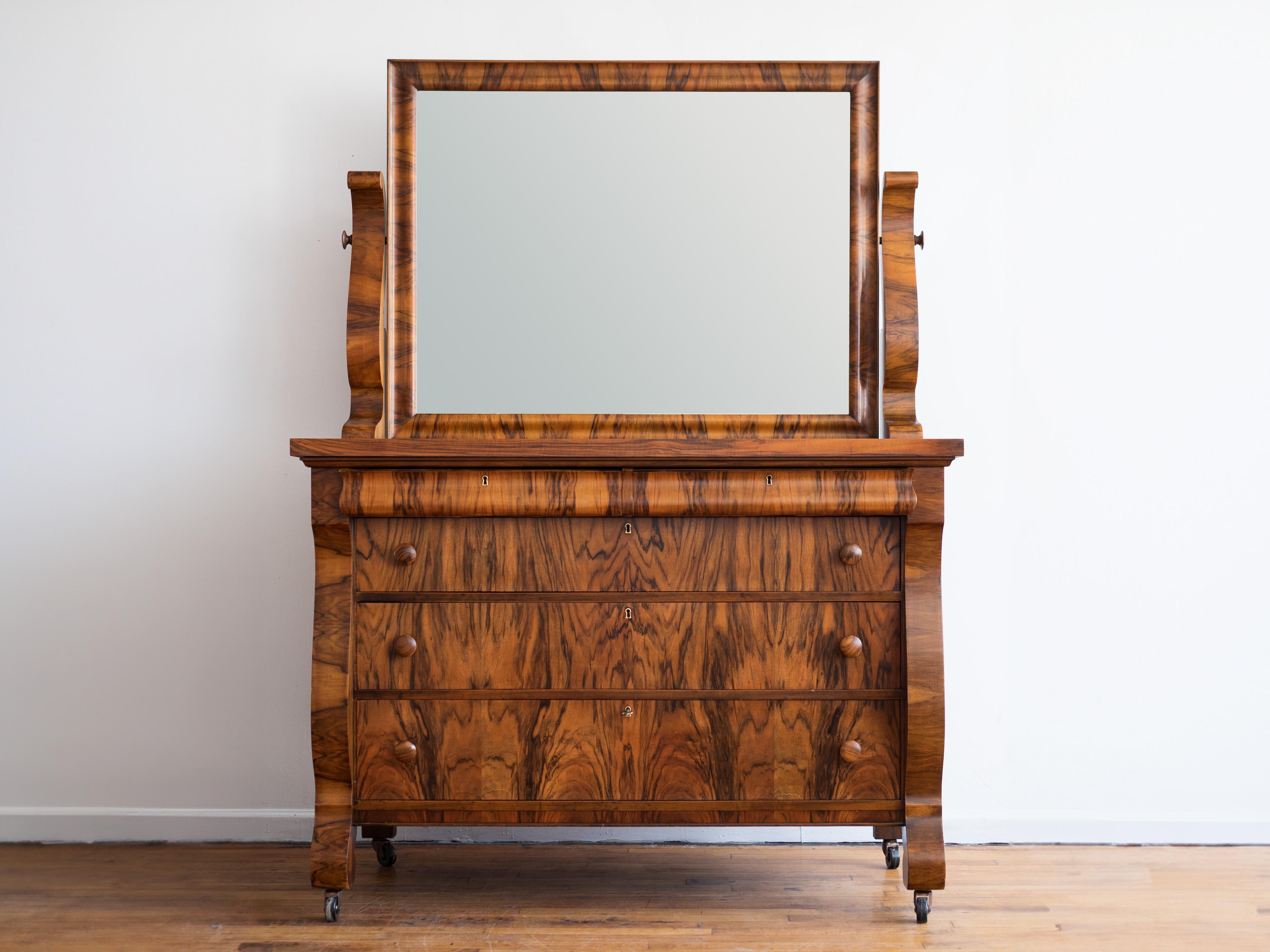 52” x 25” x 35”H (without wheels); mirror adds 35”H

A captivating representation of early Biedermeier design, influenced by the Empire era. This remarkable Biedermeier dresser exhibits an exquisite blend of aesthetics and functionality. Its