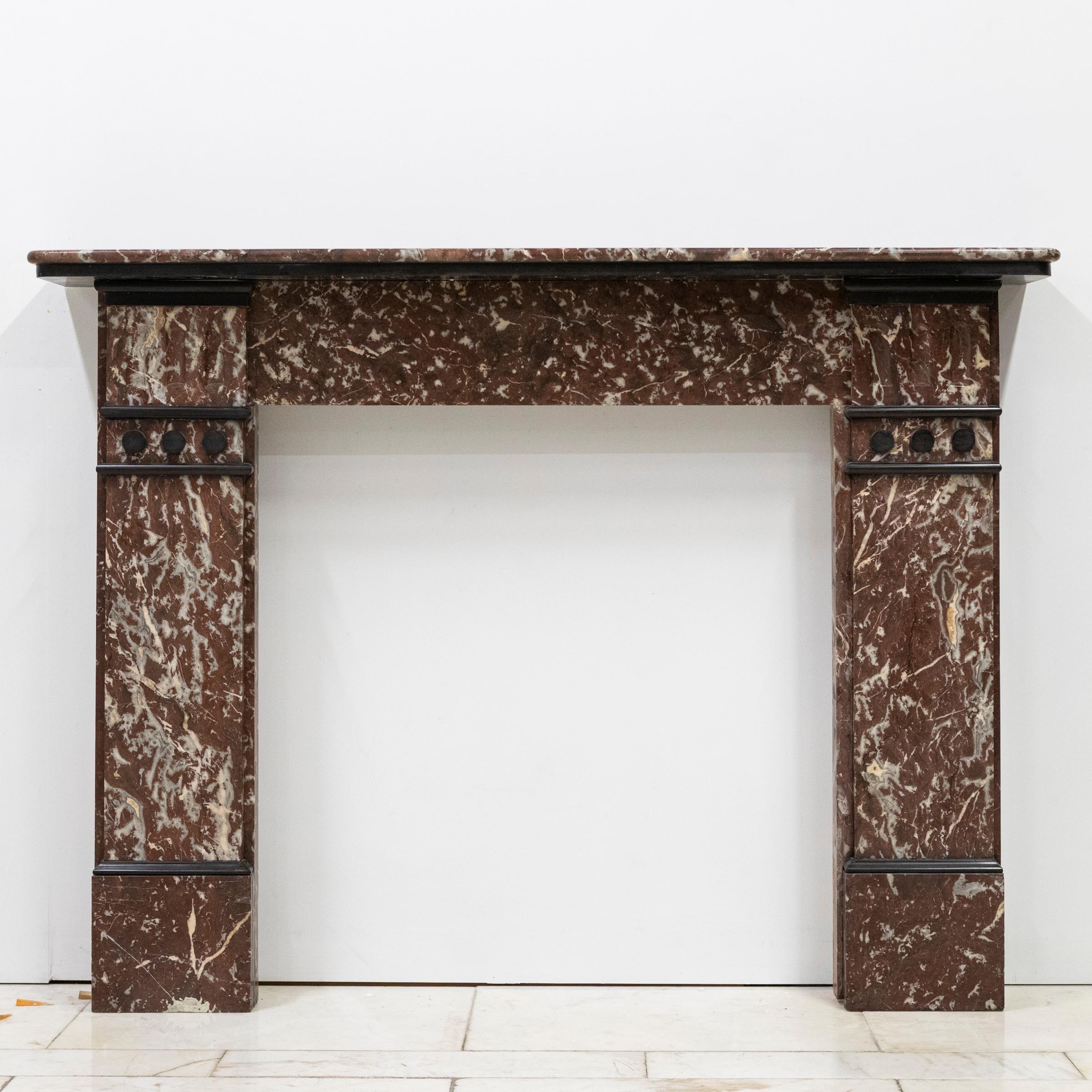 An impressive antique fireplace.

Rouge marble is contrasted against black accents in this original period chimneypiece. Carved thumbnail details surmount each jamb. A substantial bevelled shelf finishes the piece. Restored at our Hertfordshire