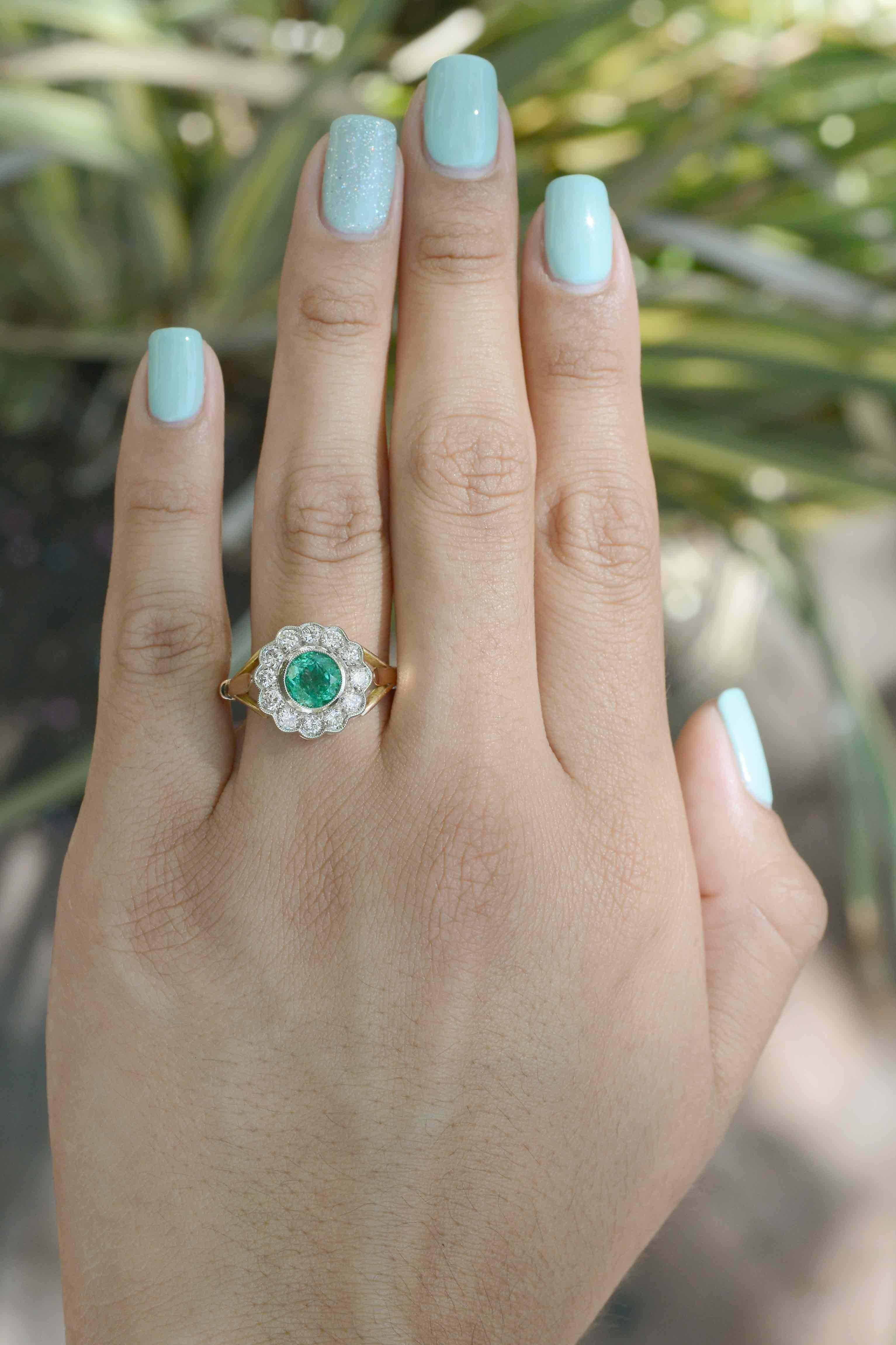 This antique emerald and diamond floral cluster engagement ring is unarguably a gorgeous, wearable piece. The enchanting emerald illuminates out of its bezel setting and is encased in a diamond floral arrangement. The setting harmonizes the soft,