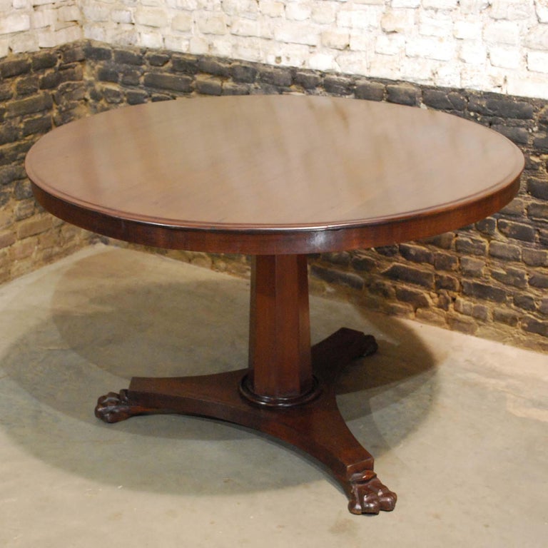 A beautiful English Regency center table with a solid mahogany top with exquisite grain and deep color. 
The top has a short mahogany veneered apron. The table stands on a tripartite base with lion’s paw feet. An octagonal tapered central column
