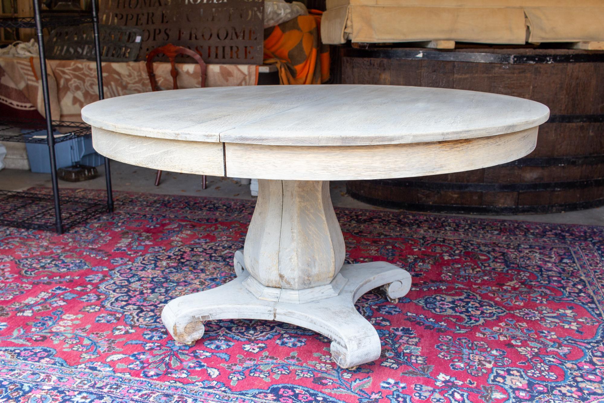 This antique round oak pedestal table has been refinished with a light greige wash and features four 10
