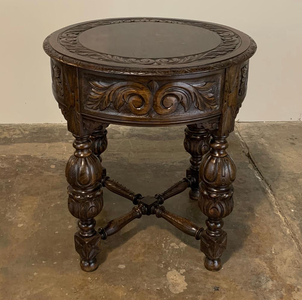 Antique round Renaissance end table features elaborate carvings around the top edge, all around the apron, and even on the four urn-shaped legs, which are connected with an 