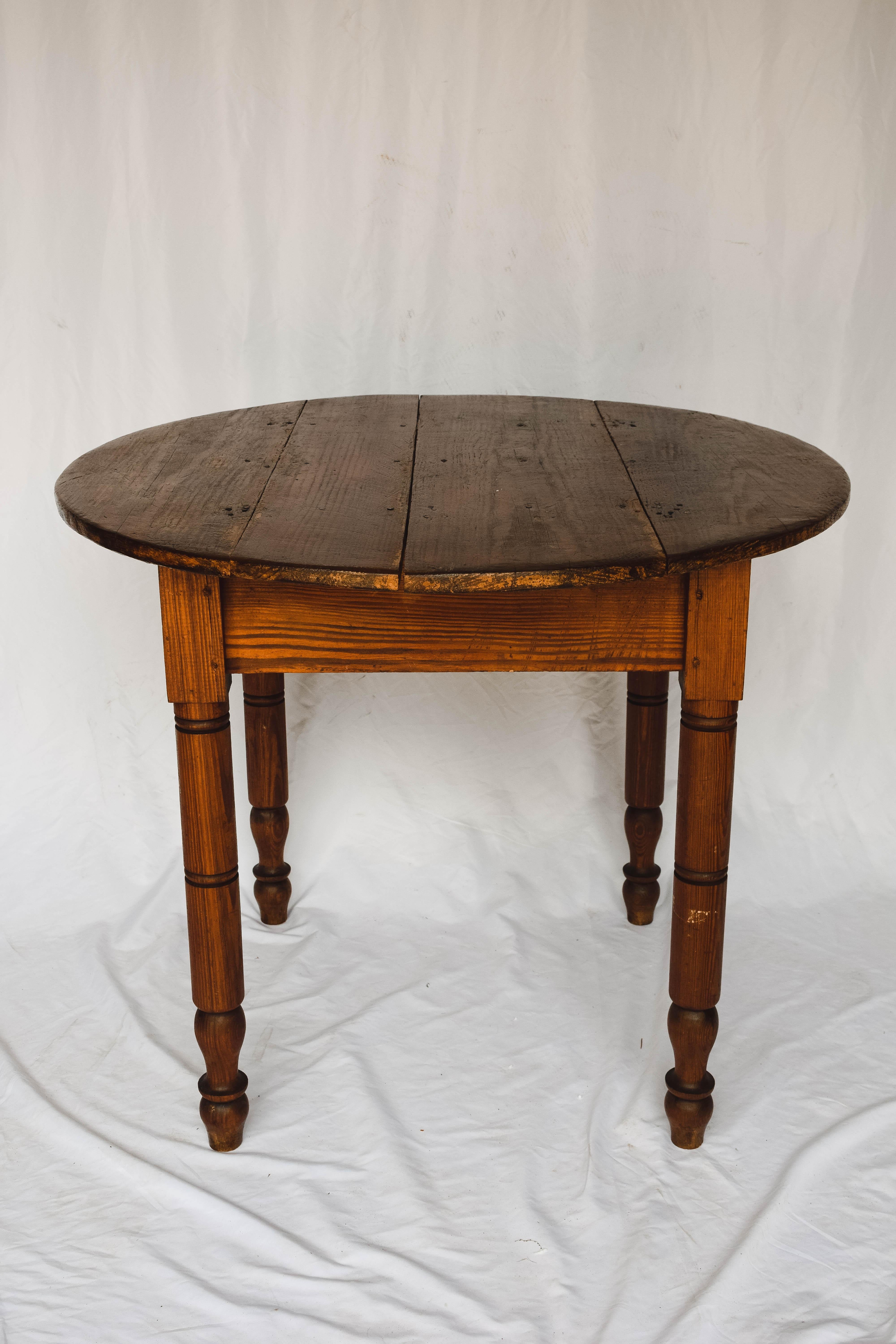 This antique round Tavern table is constructed with a plank top and sits on four turned legs. The top is removable for ease of mobility.