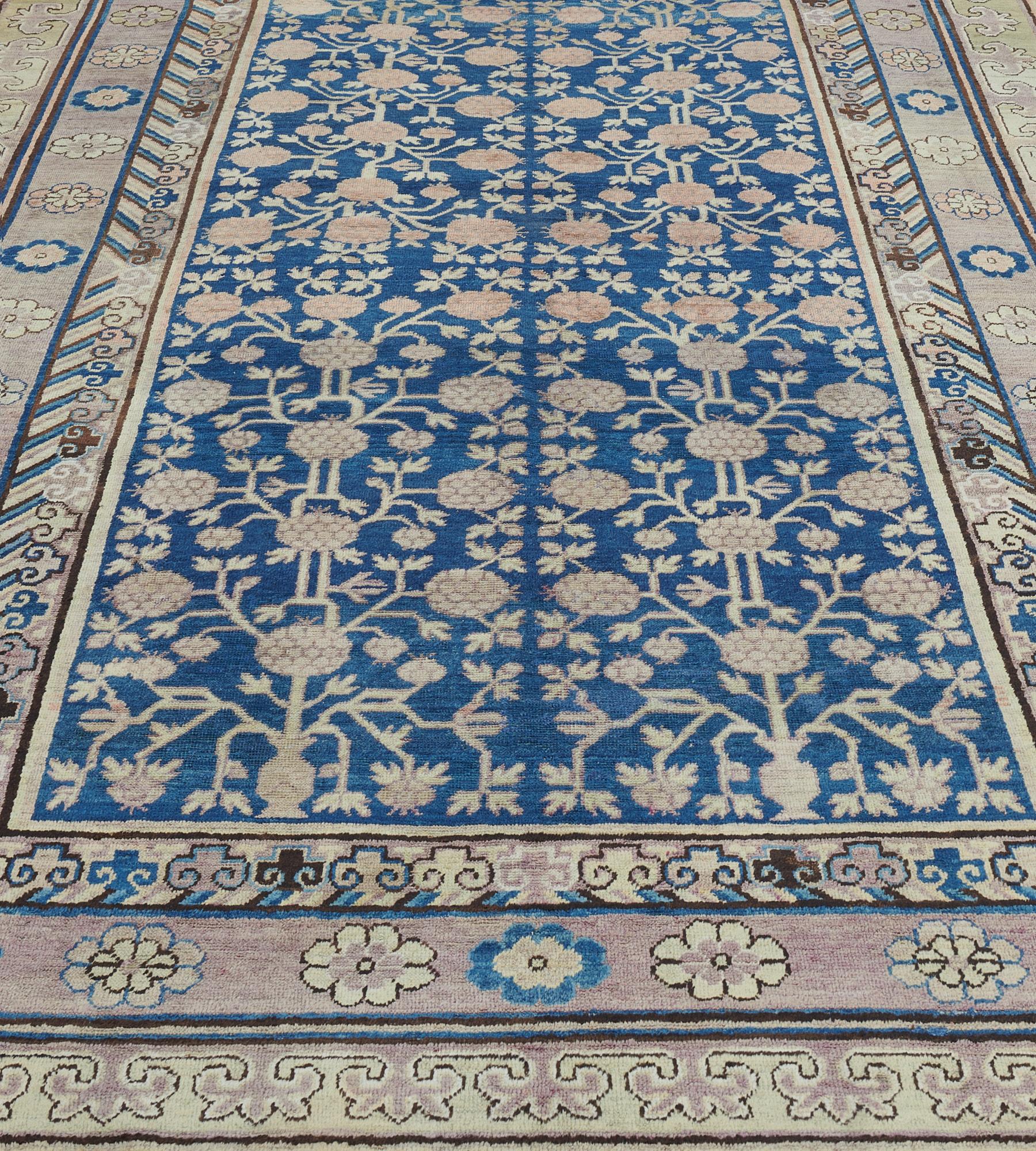 Dieser antike Khotan-Teppich hat ein königsblaues Feld mit einem Granatapfel-Gitter in einer pflaumenfarbenen Rosettenbordüre zwischen beigen Wolkenmotiven und geometrischen Bordüren, flankiert von tabak- und marineblauen Streifen.