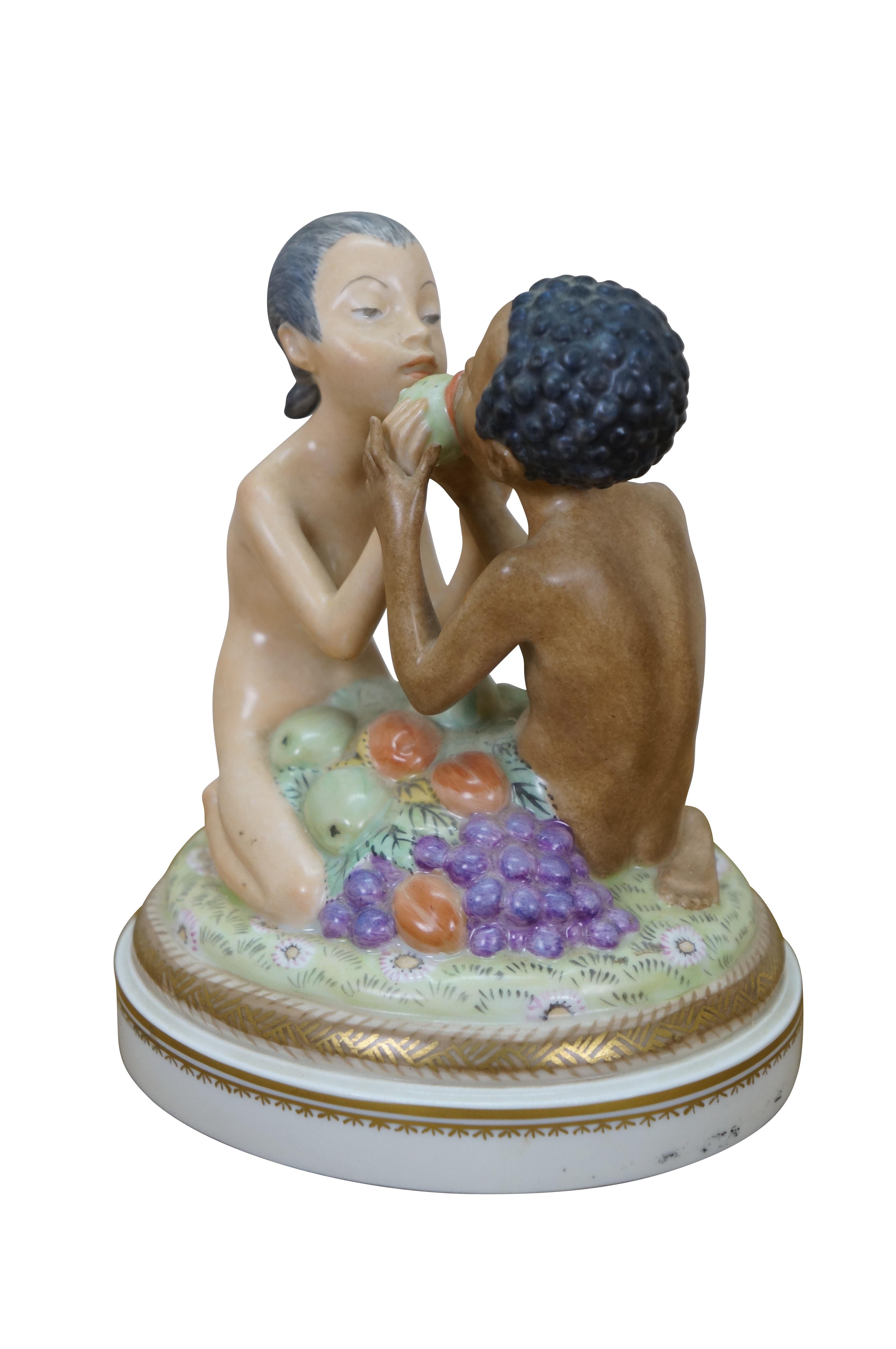 Antique Adam & Eve porcelain figurine designed by Hans Henrik Hansen for Royal Copenhagen.  Designed by HHH in 1919, model #1997.  Depicts Adam and Eve seated in a pile of forbidden fruit, sharing a prickly pear; round base with gilt snake edging. 