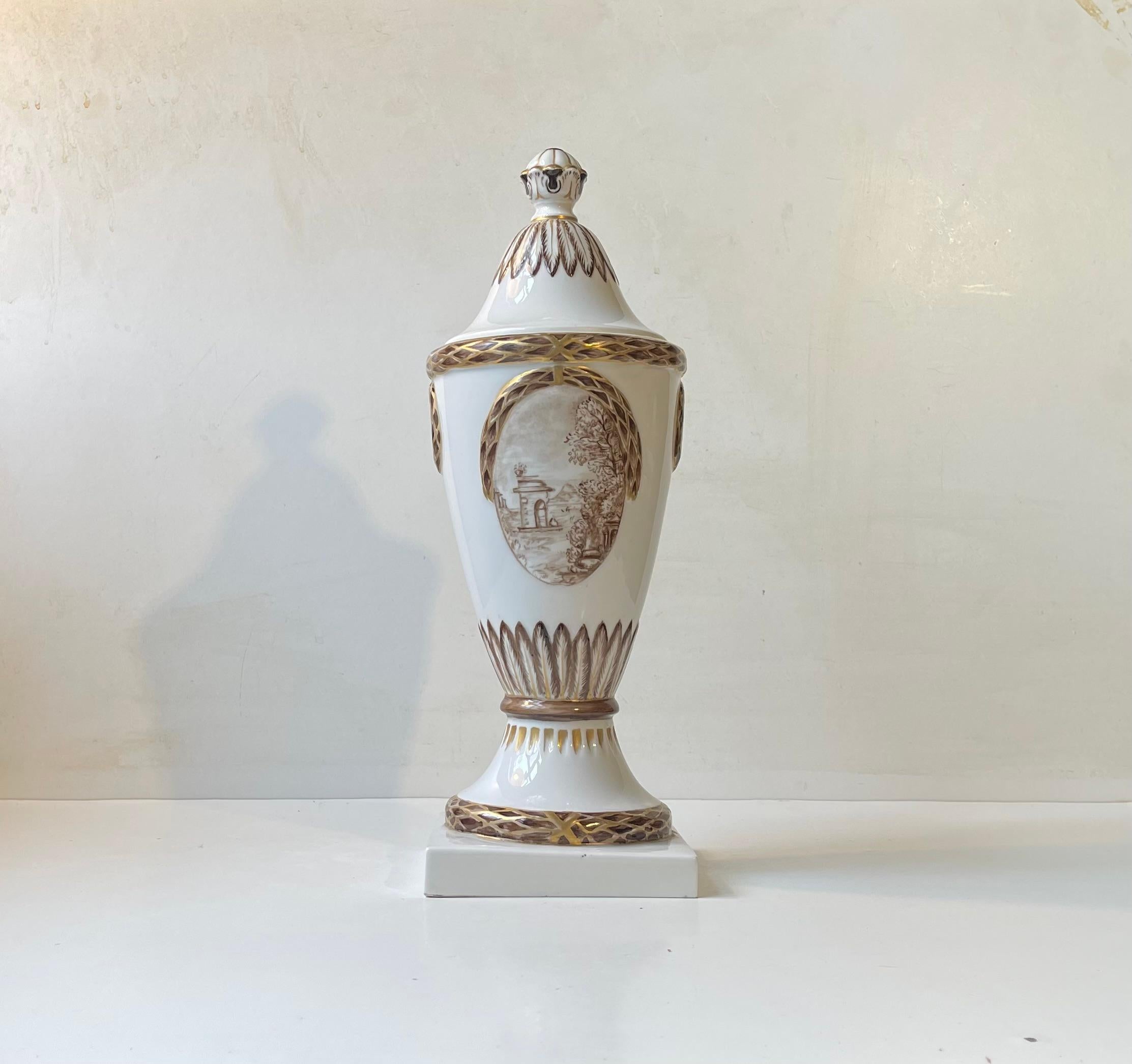 A late 19th century or early 20th century porcelain urne decorated with gold and brown over-glazing and featuring to motifs. An idyllic Danish scene and a bouquet of flowers hand-painted in a brown/rose sepia color. It has Royal Copenhagen markings