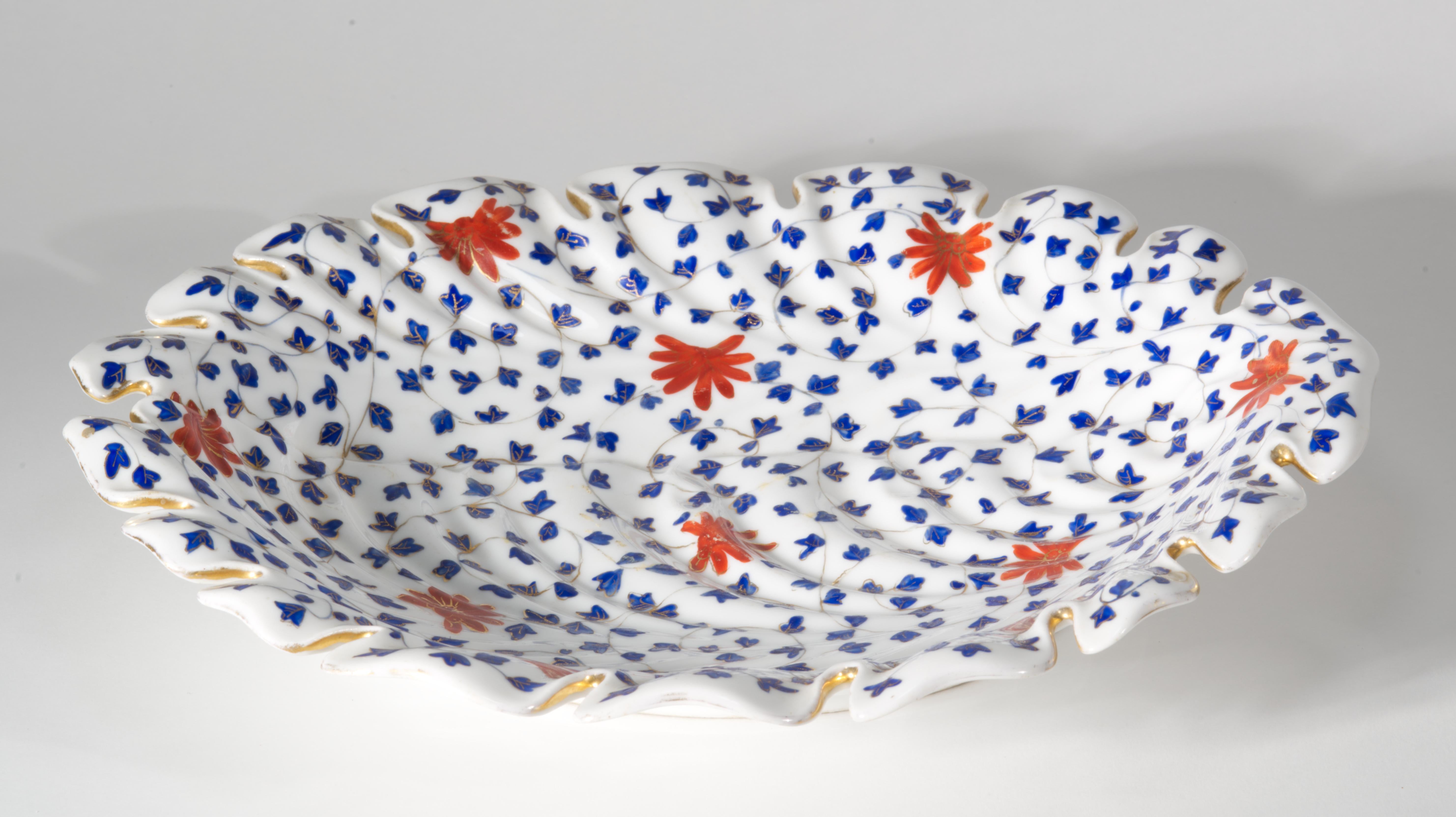 Rare, unusual footed serving platter features elaborate hand-painted decor on highly textured porcelain blank. Leaf-shaped platter has an asymmetrical ornate rim; the elements of the rim continue as textured ridges, flowing along the surface of the