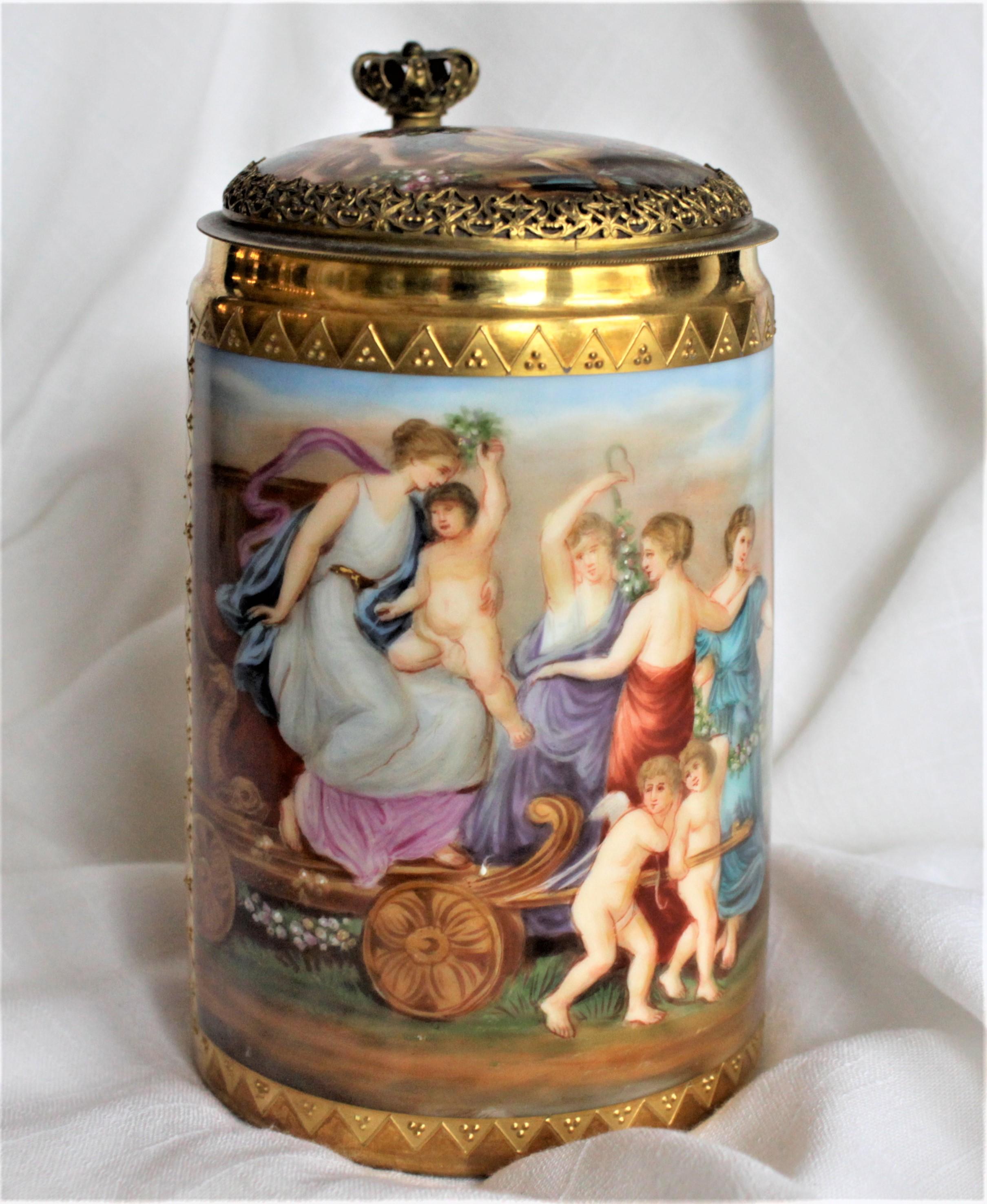 This antique and elaborately hand painted porcelain tankard is believed to have been made in Europe in circa 1880 in the neoclassical style of Royal Vienna. This covered stein has a highly detailed hand painted panel of the Wagon of Venus on the