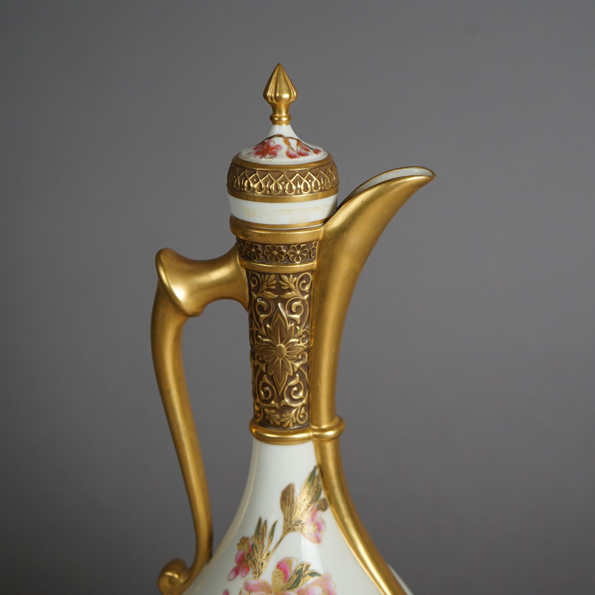 An antique English Royal Worcester Egyptian Revival lidded and footed ewer offers porcelain construction with exaggerated neck, hand painted garden flowers & butterflies, and heavily gilt throughout; maker mark on base as photographed;