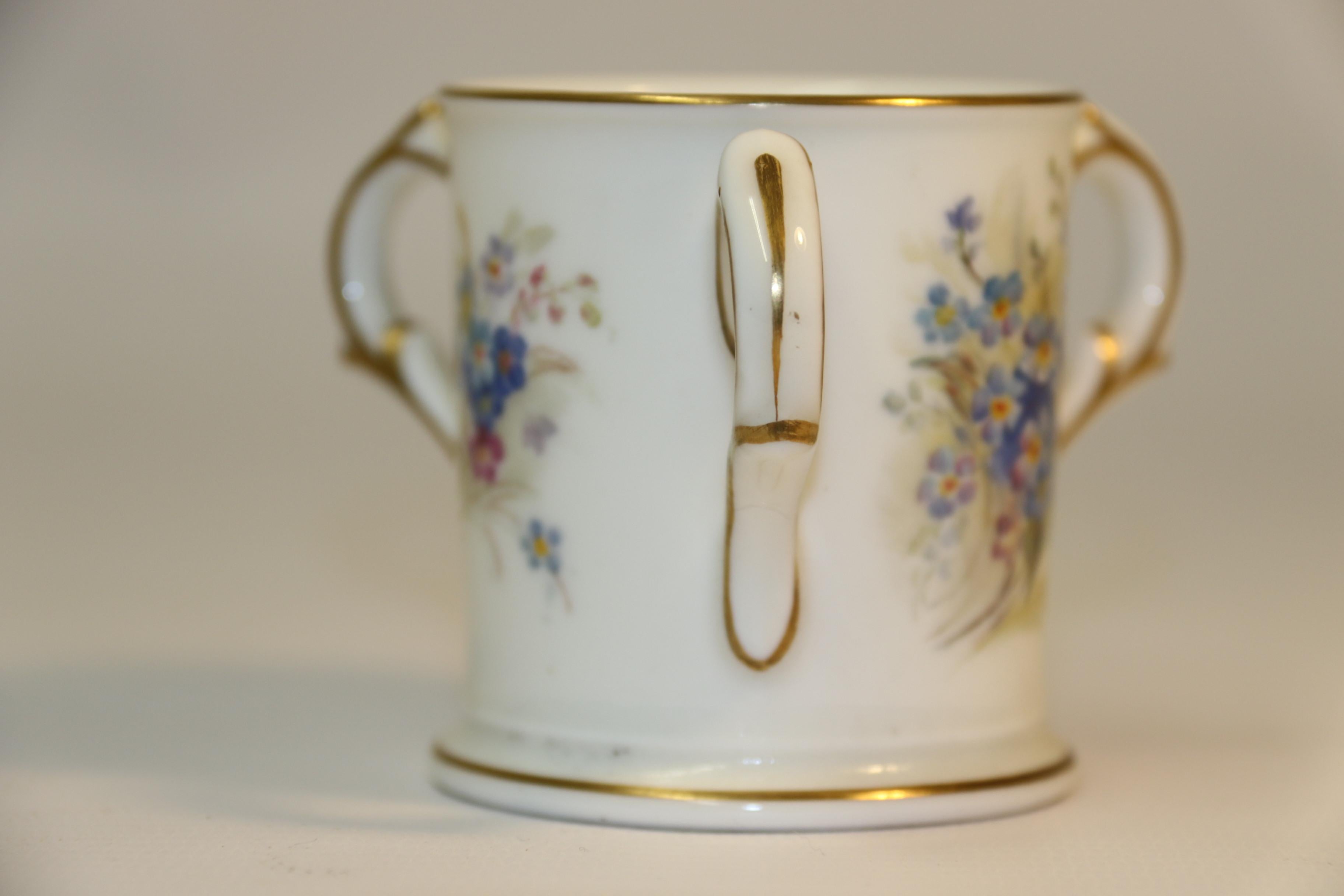 This delightful early 20th century Royal Worcester porcelain miniature loving cup has a white ground with fabulous hand painted sprays of forget-me-nots. These are centralised between the three handles which are decorated with gilt lines as is the