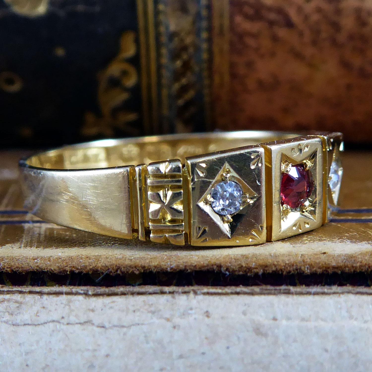 A Victorian ring crafted in 18ct yellow gold and set to the centre with a round mixed cut ruby bead set into a pinched square mount on a square plaque.  The ruby is flanked to either side with an old cut diamond bead set to a diamond shaped mount on