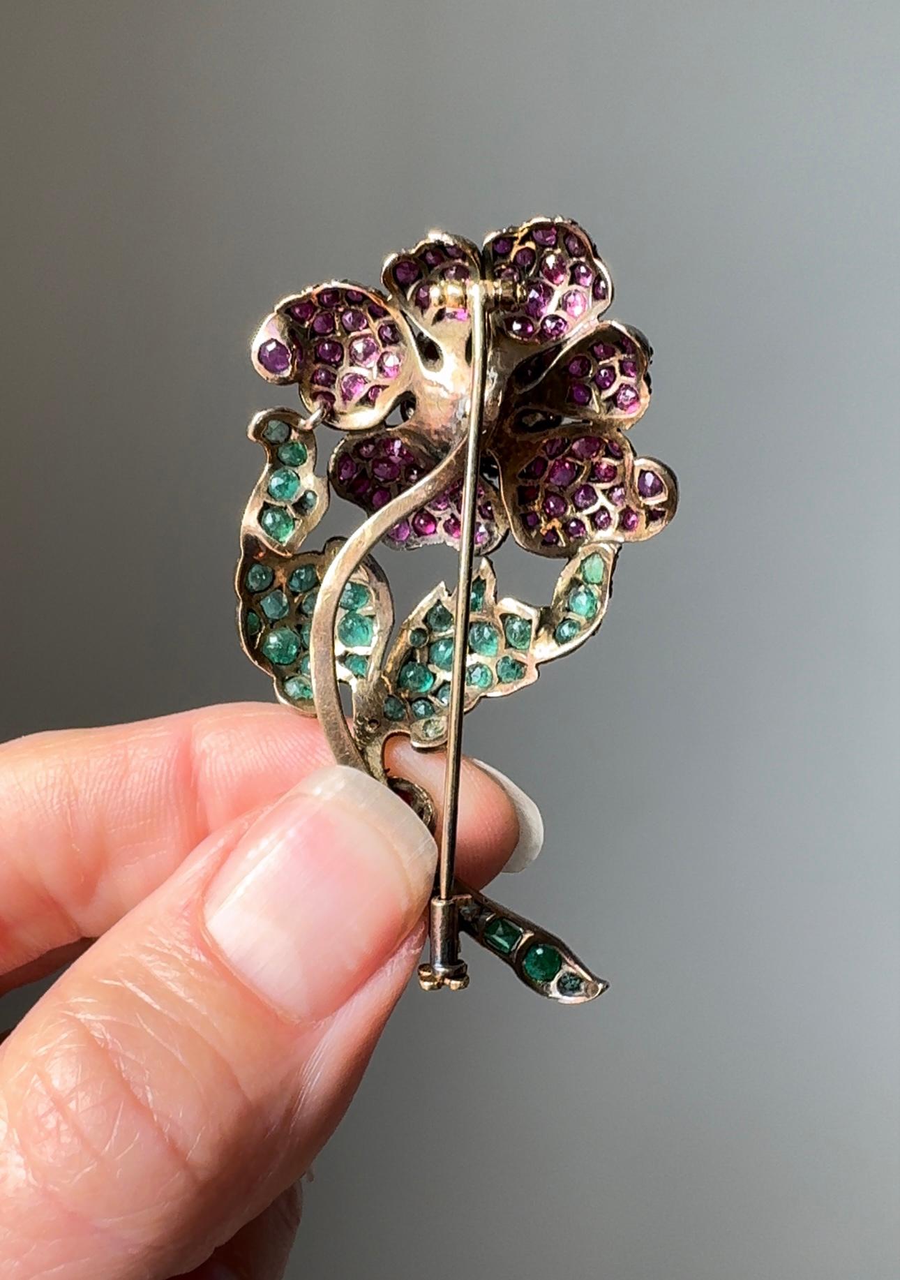 Fit for a queen, this timelessly elegant late 19th century rose is designed with delicately curled petals filled with vibrant raspberry red rubies complimented by bright green emerald leaves, expertly hand fabricated silver topped gold.

