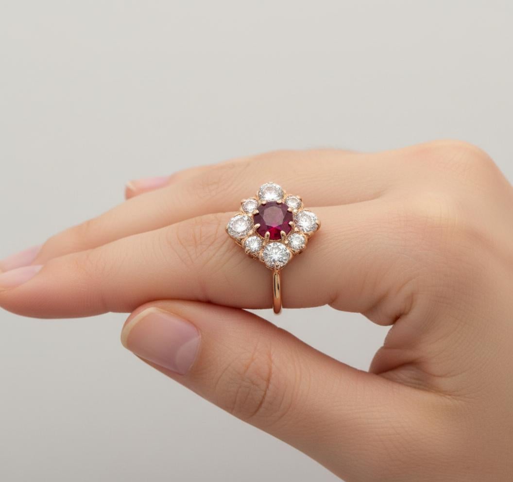This exquisite 14kt antique ring features a vibrant oval ruby weighing 1.30 carats, characterized by its bright red hue.    Surrounding the ruby are eight Old European cut diamonds, totaling 1.50 carats, arranged in a graduated frame that