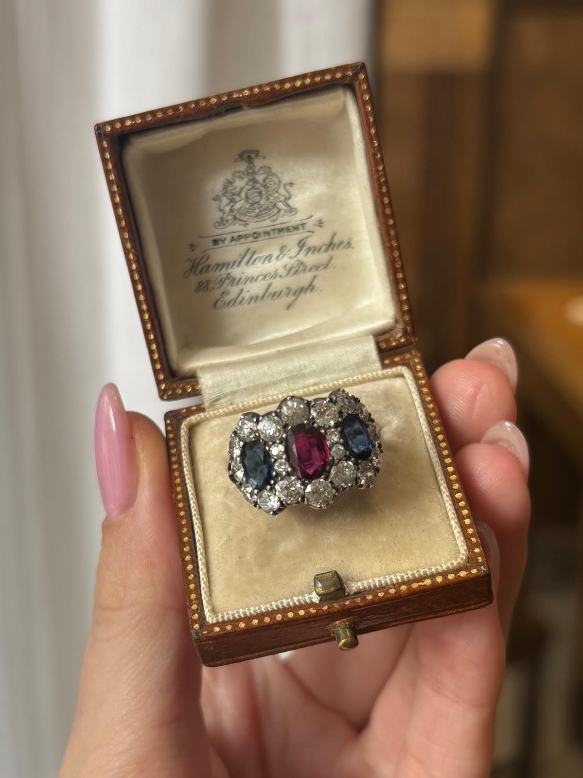 Anillo antiguo de rubí, zafiro azul y diamante talla antigua de oro de 18 quilates y plata. 

El anillo está engastado en el centro con un impresionante rubí de forma ovalada, engarzado en una garra con la parte posterior abierta. El rubí está