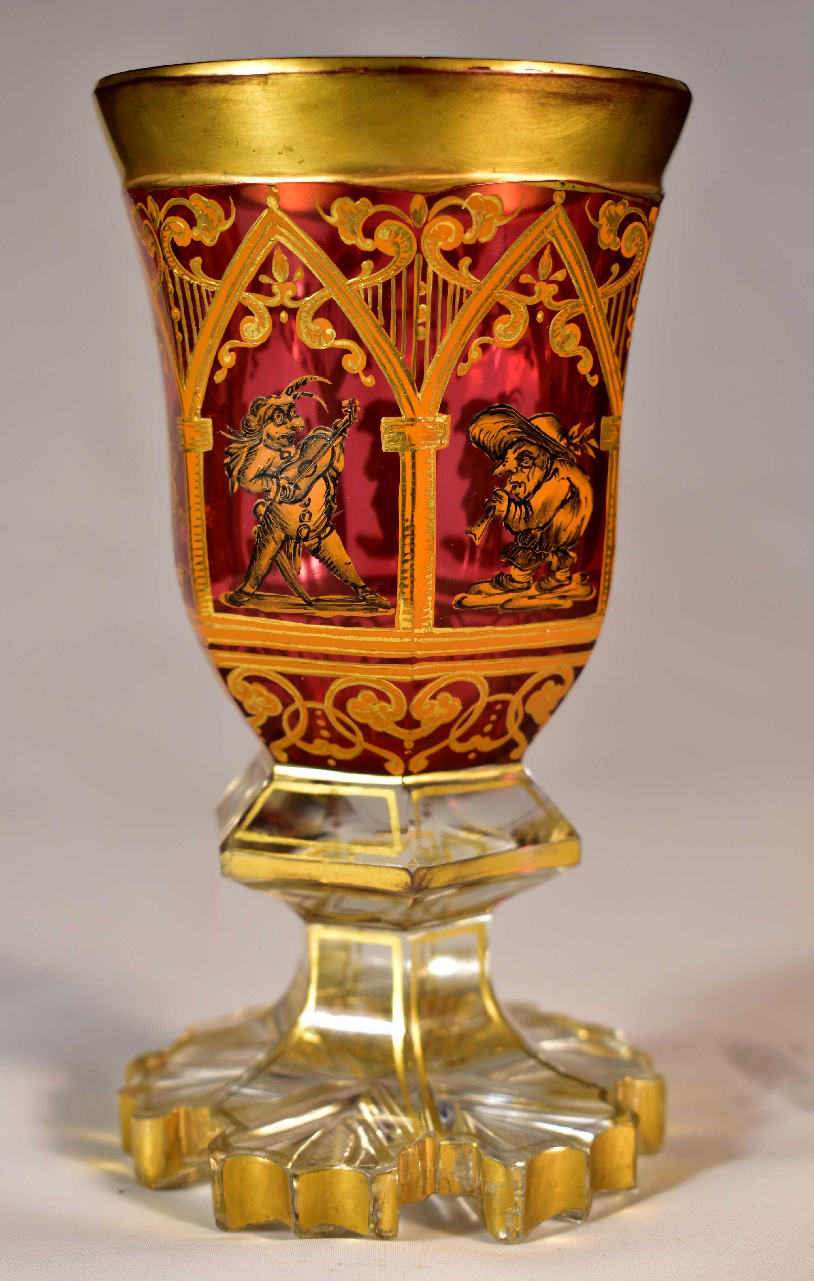 A beautiful ruby goblet with a clear foot, cut and painted, The portals are painted in ocher color and everything is complemented by gilding, In the Portals, there are painted figures of musician sprites. The bottom of the goblet is especially