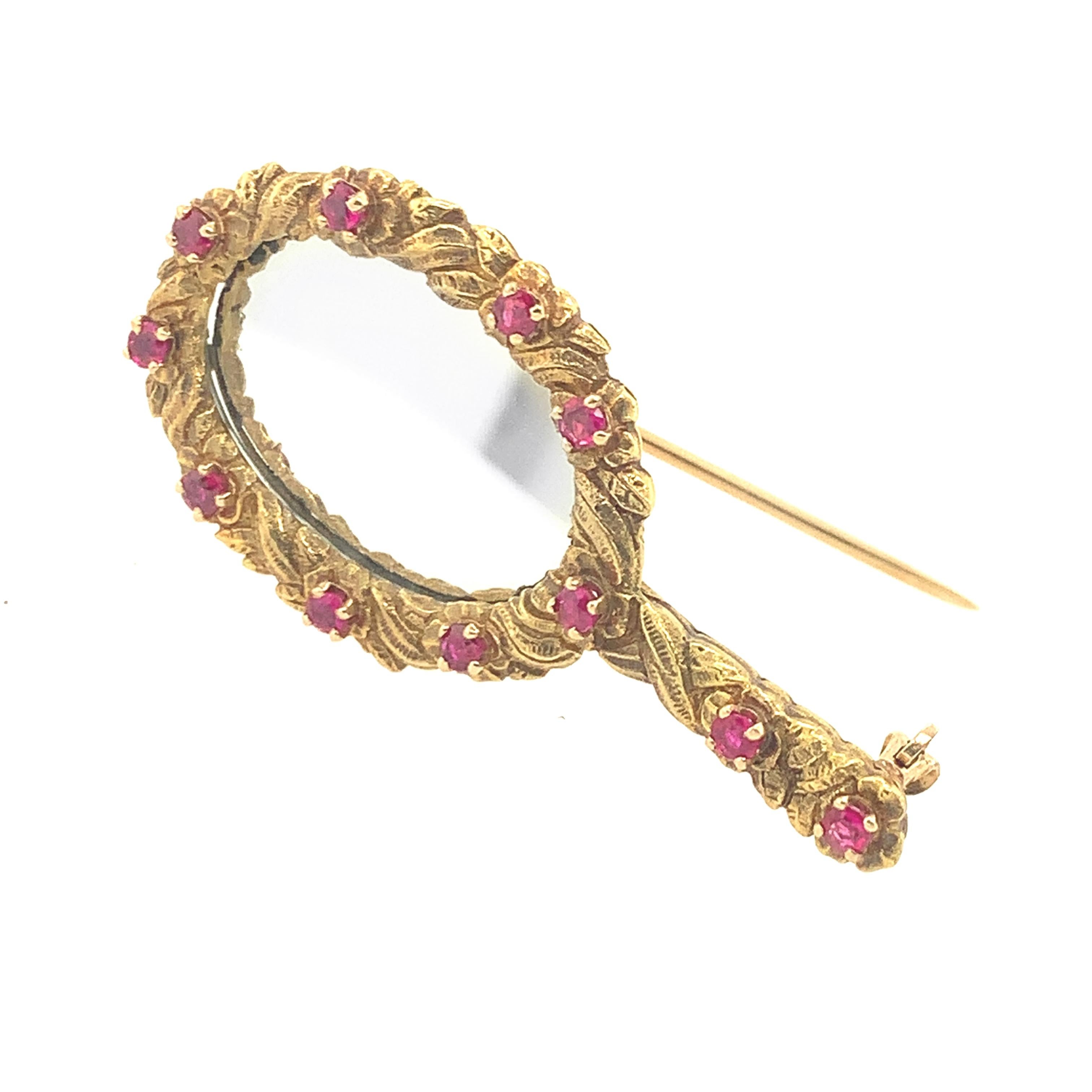 A fabulous figural mirror pin: beautifully hand-crafted with a central reflective mirror surrounded by an engraved garland of figural flowers accentuated with 11 sparkling round brilliant rubies.  14K yellow gold.  Perfect for day to dress. 