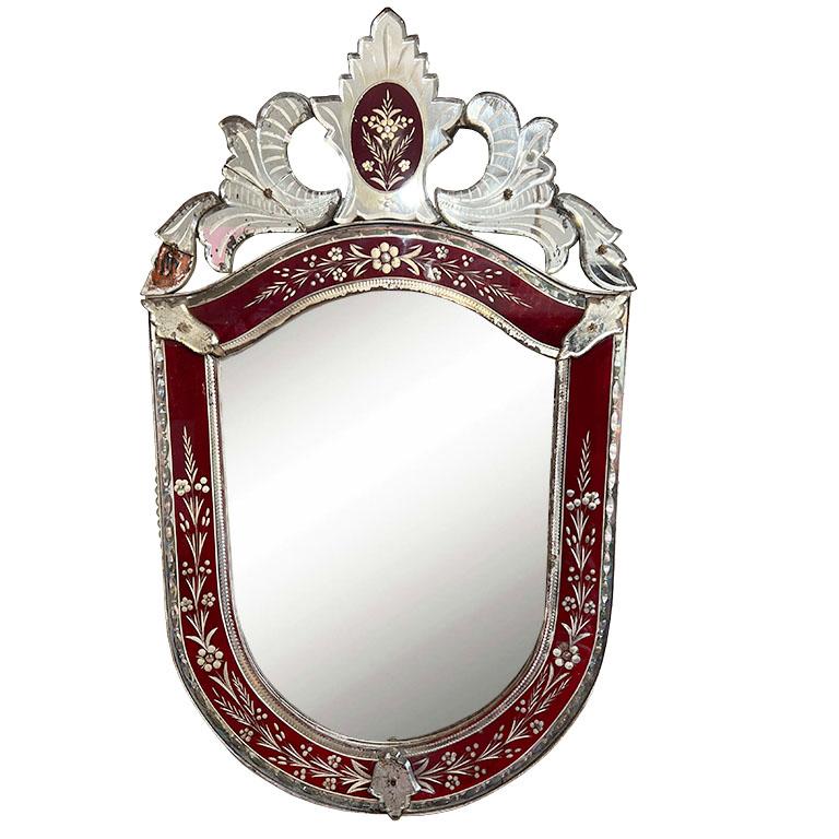 A beautiful Venetian mirror in ruby red. The mirror is U-shaped, and features applied and etched pieces of mirror in various stylized shapes. Most Venetian mirrors are made in Italy, however, this one is special and was made in France. The back of