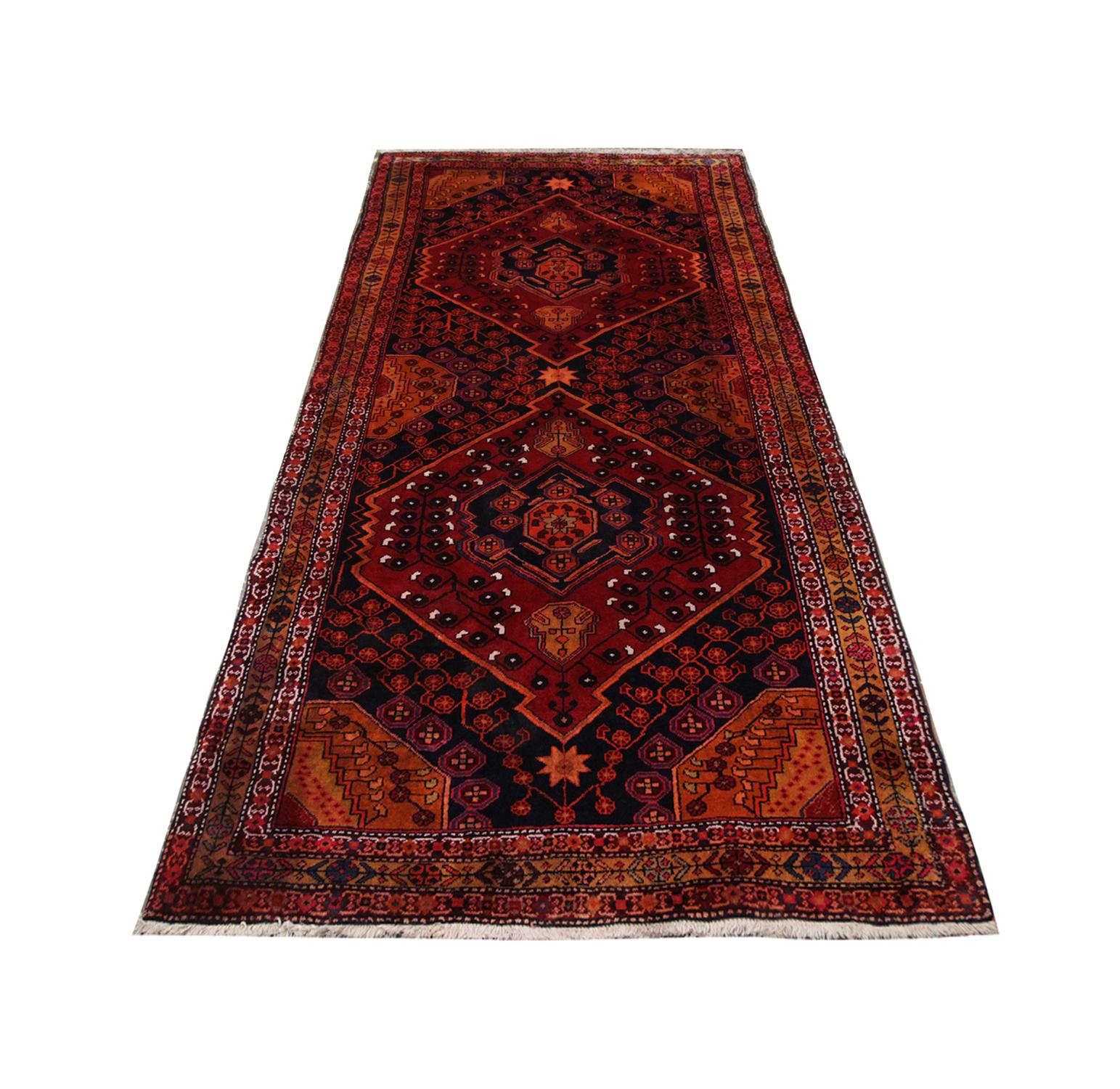 Deep reds and burnt oranges have been used to hand knot this stunning area rug. Two diamond-like shapes sit in the centre of this rug as the main emblems. It is designed with intricate details throughout the centre panel and borders. Subtle hints of