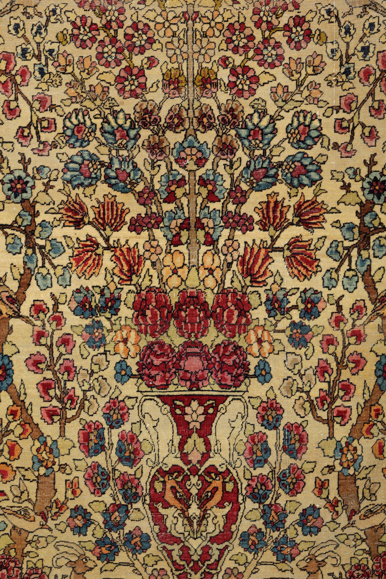 This rare wool rug is a fine example of an antique carpet woven in the 1870s. The design features an intricately woven vase. Highly-detailed floral and botanical arrangements flow from the top of the vase woven in orange, blue and red accents on an