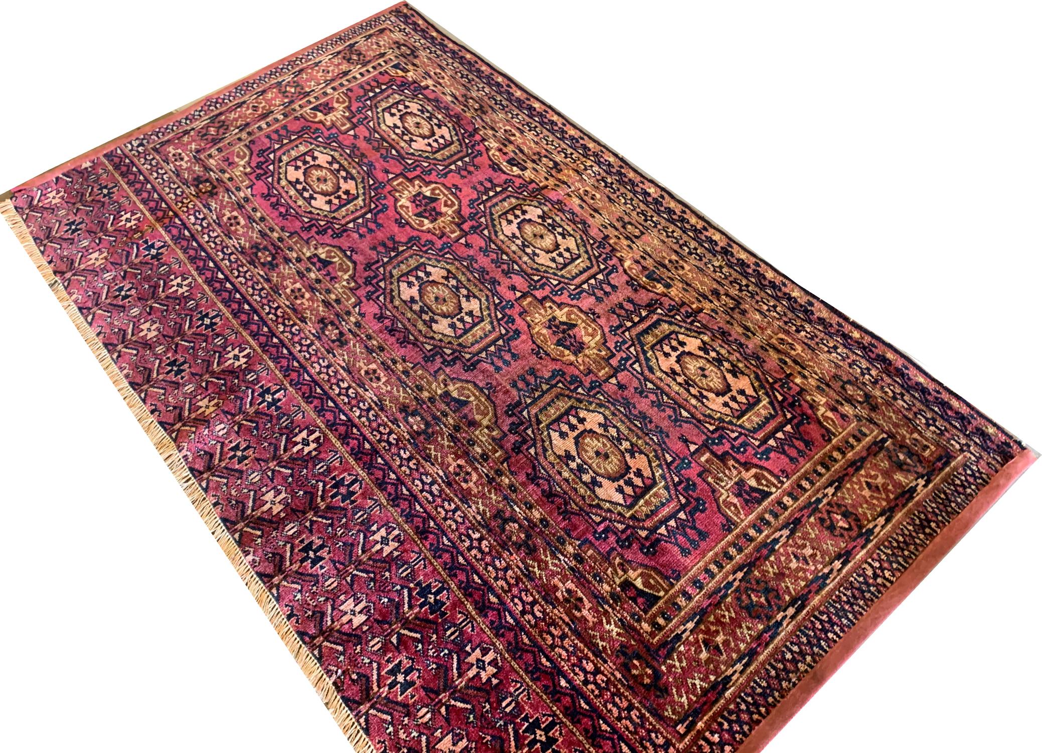 A geometric tribal design has been woven on a rich pink-Rust background in accents of blue, orange, beige and brown. This piece is an antique Asian carpet woven in the 1880s with sophistication and features traditional motifs and patterns. The