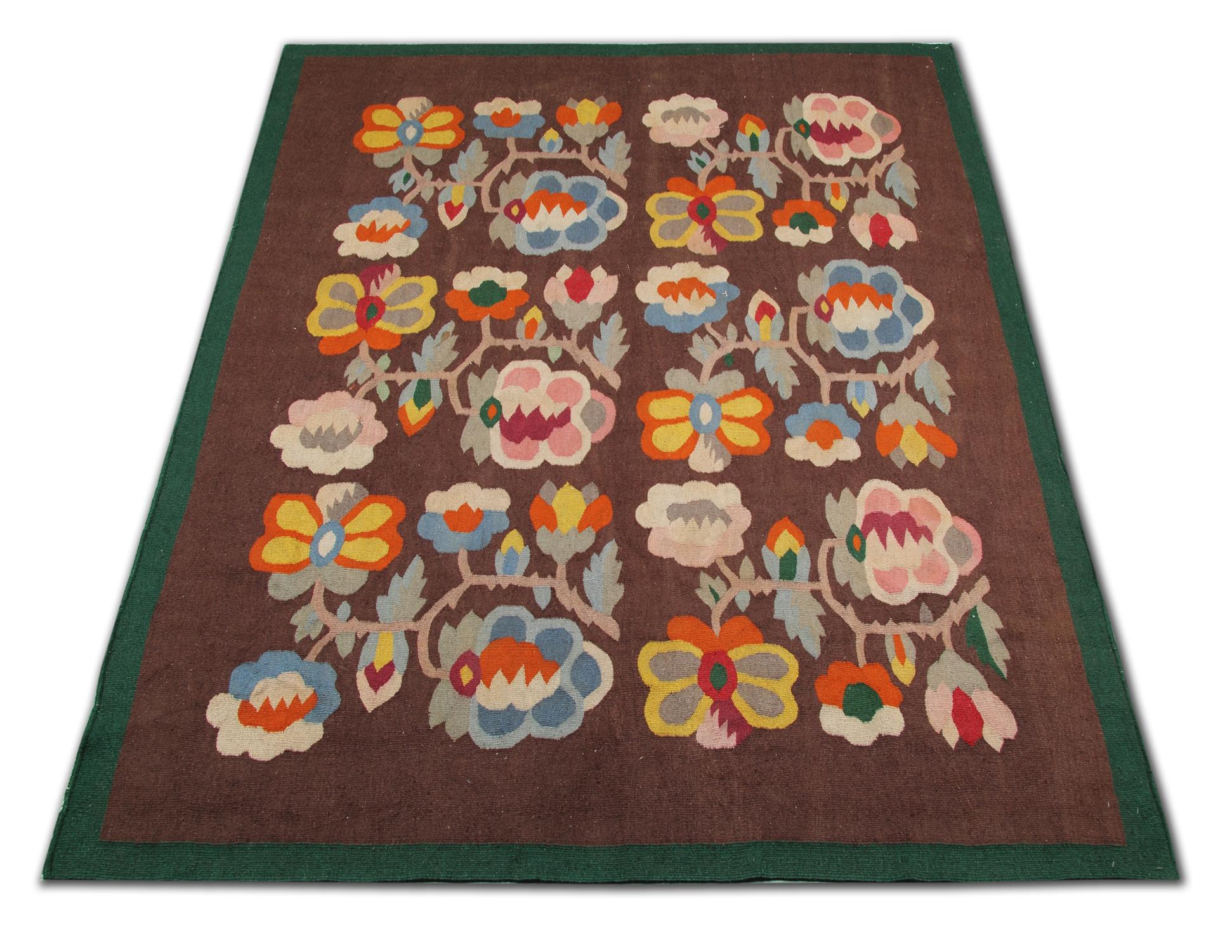 This brown floral wool area rug was made by hand in Romania in the 1920s and featured a repeat pattern floral motif design. They featured six floral medallions woven in accents of blue, beige, pink and cream on a brown background. A simple green