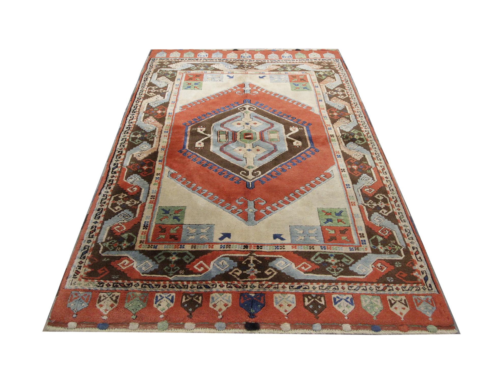 This antique Turkish rug from Milas area and was handwoven with tribal and geometric symbols in circa 1930. The design features a large multicolored motif as the central medallion on a burnt orange diamond shape background. The captivating border