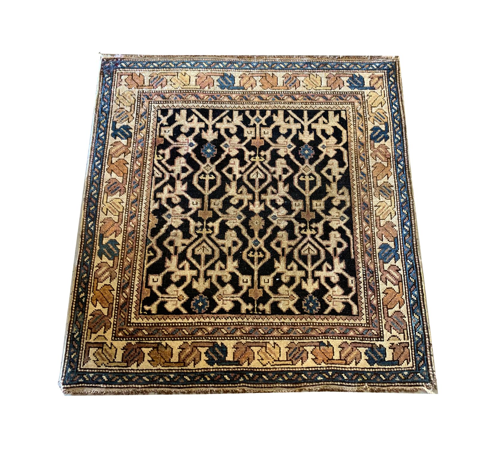 This small square rug was woven by hand in Kuba. The design is sophisticated, woven with a bold black background with contrasting accents of cream, beige, blue and brown that make up the symmetrical all-over pattern. This has then been framed by a