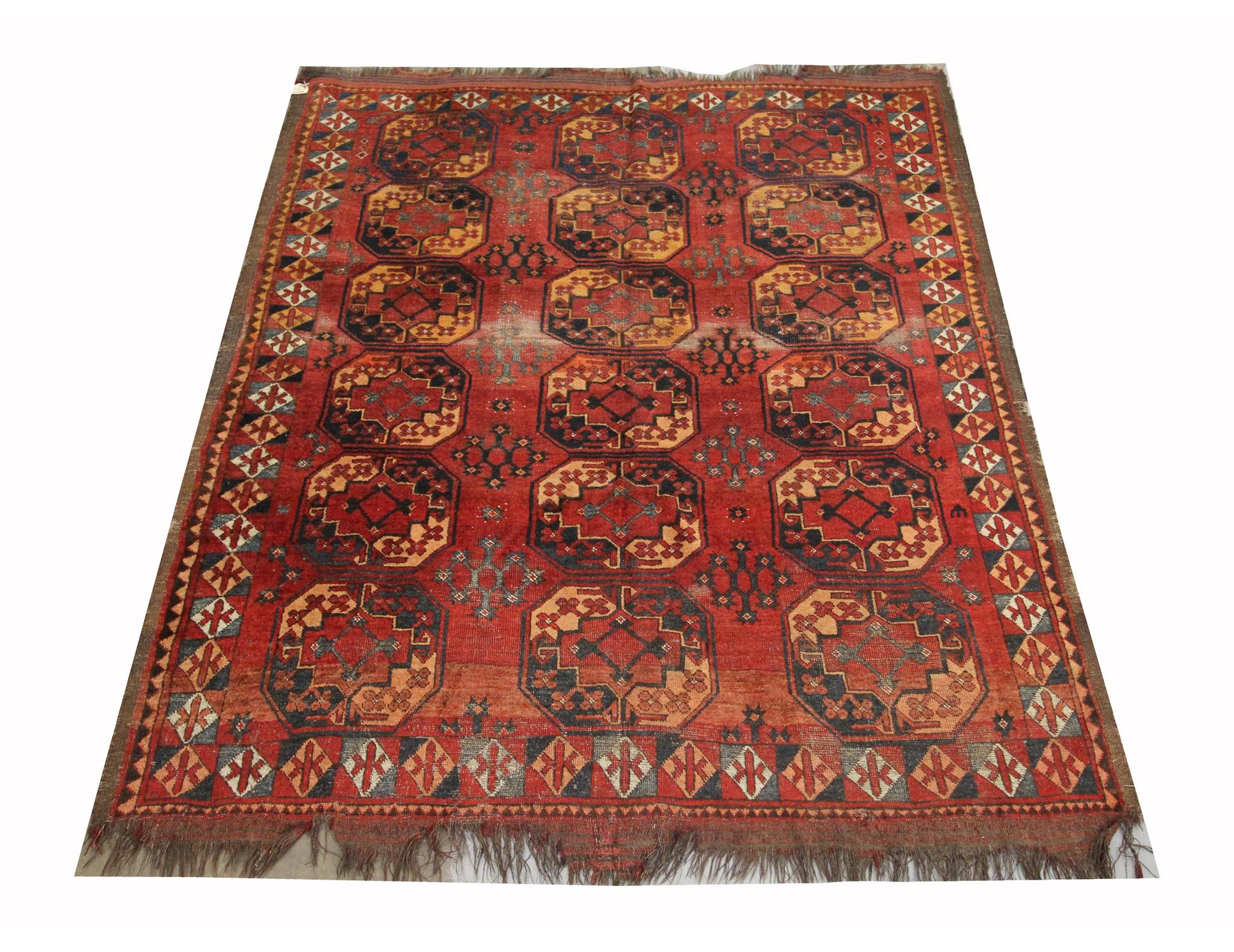 This antique piece is a Turkmen Ersari rug woven by hand in the 1880s. The central design features a rust background with a repeating traditional Turkmen medallion pattern that has been woven in accents of orange and grey/black. The intricate