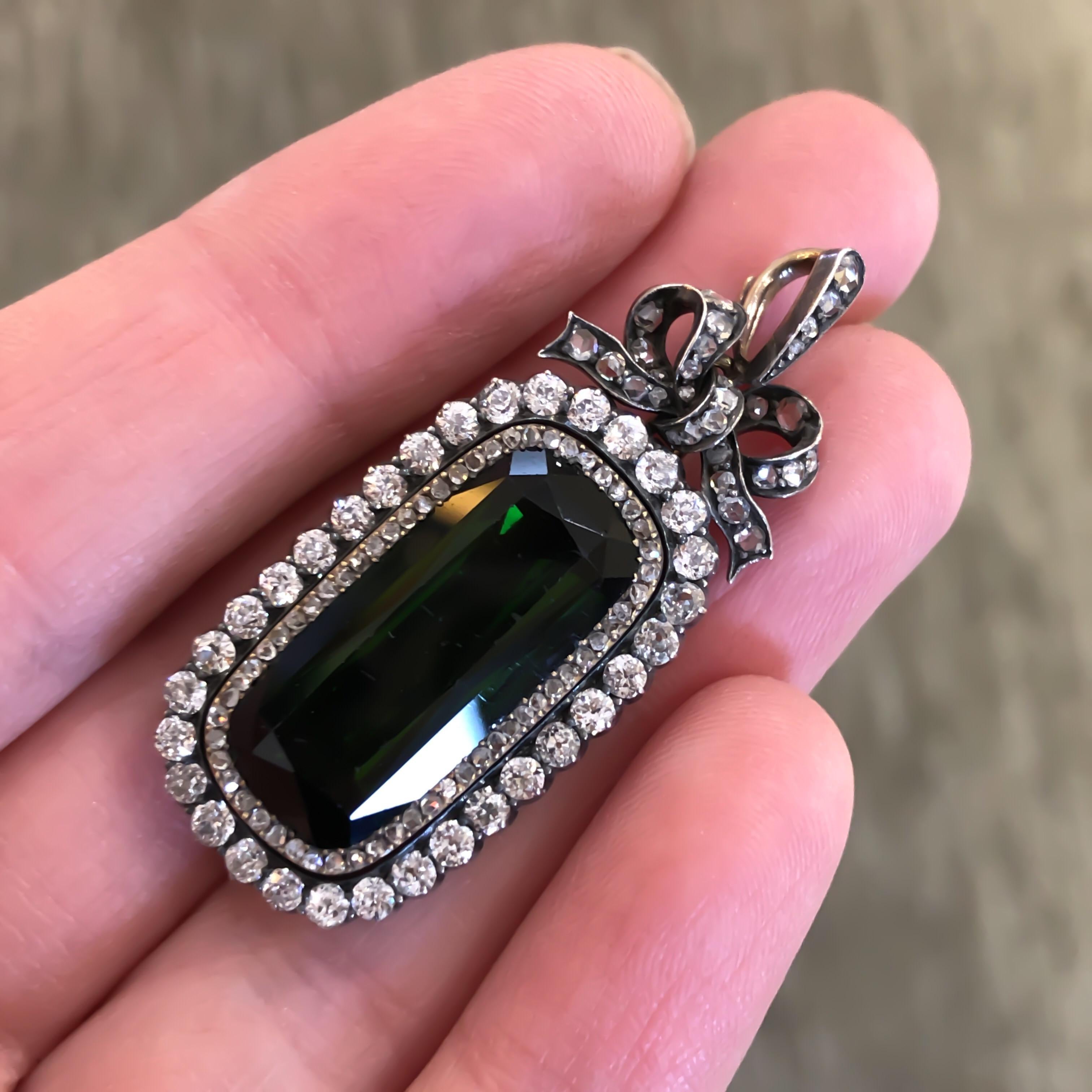 Antique Russian pendant/brooch made in 18K yellow gold and silver.  Two rows of old mine cut diamonds circle one elongated oval scissor cut green Tourmaline, they also decorate a bow and bail at the top. The bow and bail are removable. The