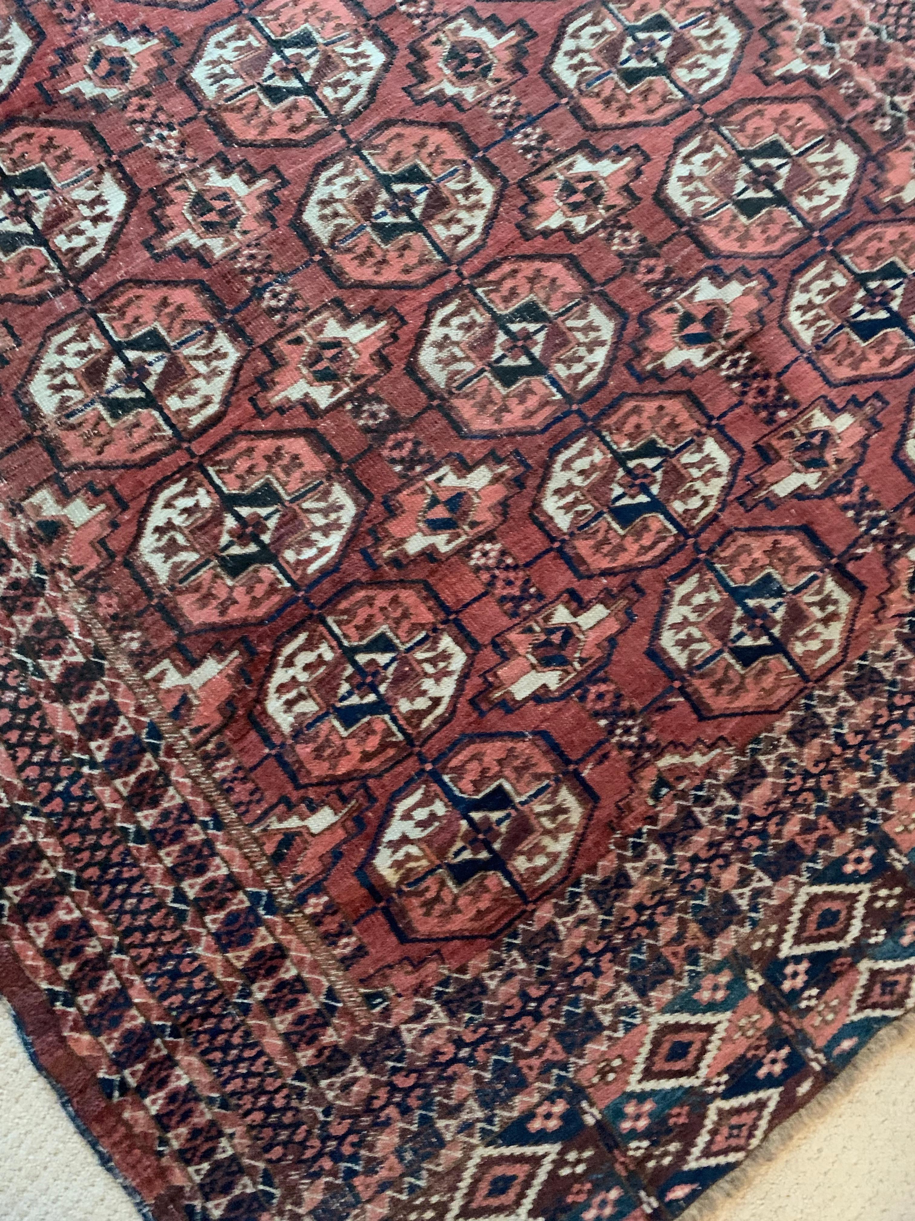A Bokhara rug from the Caucasus region of the early 20th century with geometric gulls and polygons with a red background and shades of blue and beiges. Tribal motifs with Classic borders.