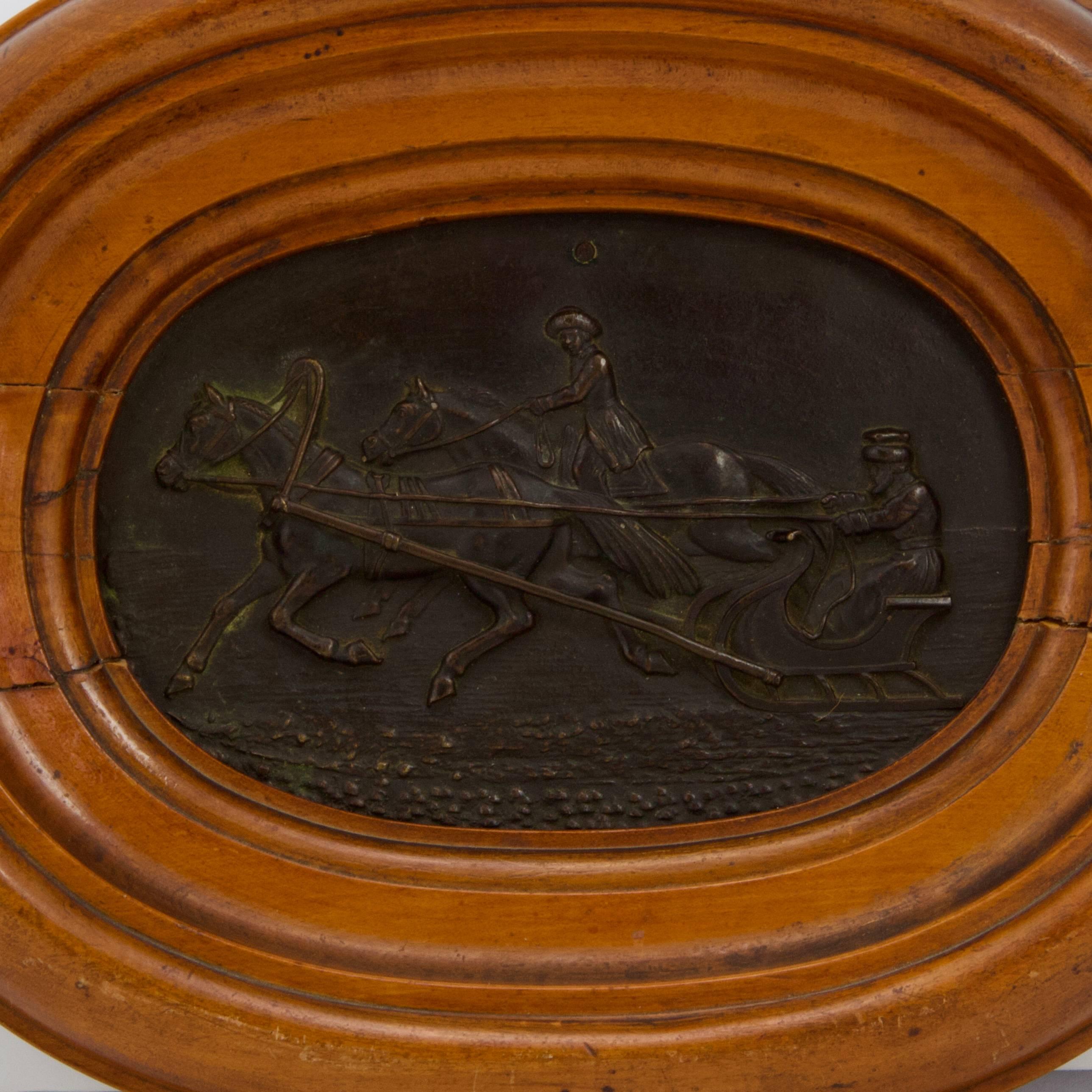 Oval bronze representing a troika driving to the forefront and on a backdrop an horse rider. Originally with an hole. Dark patina.
Now bordered in a large and deep honey-colored wood frame.
Frame showing antique restoration.
No