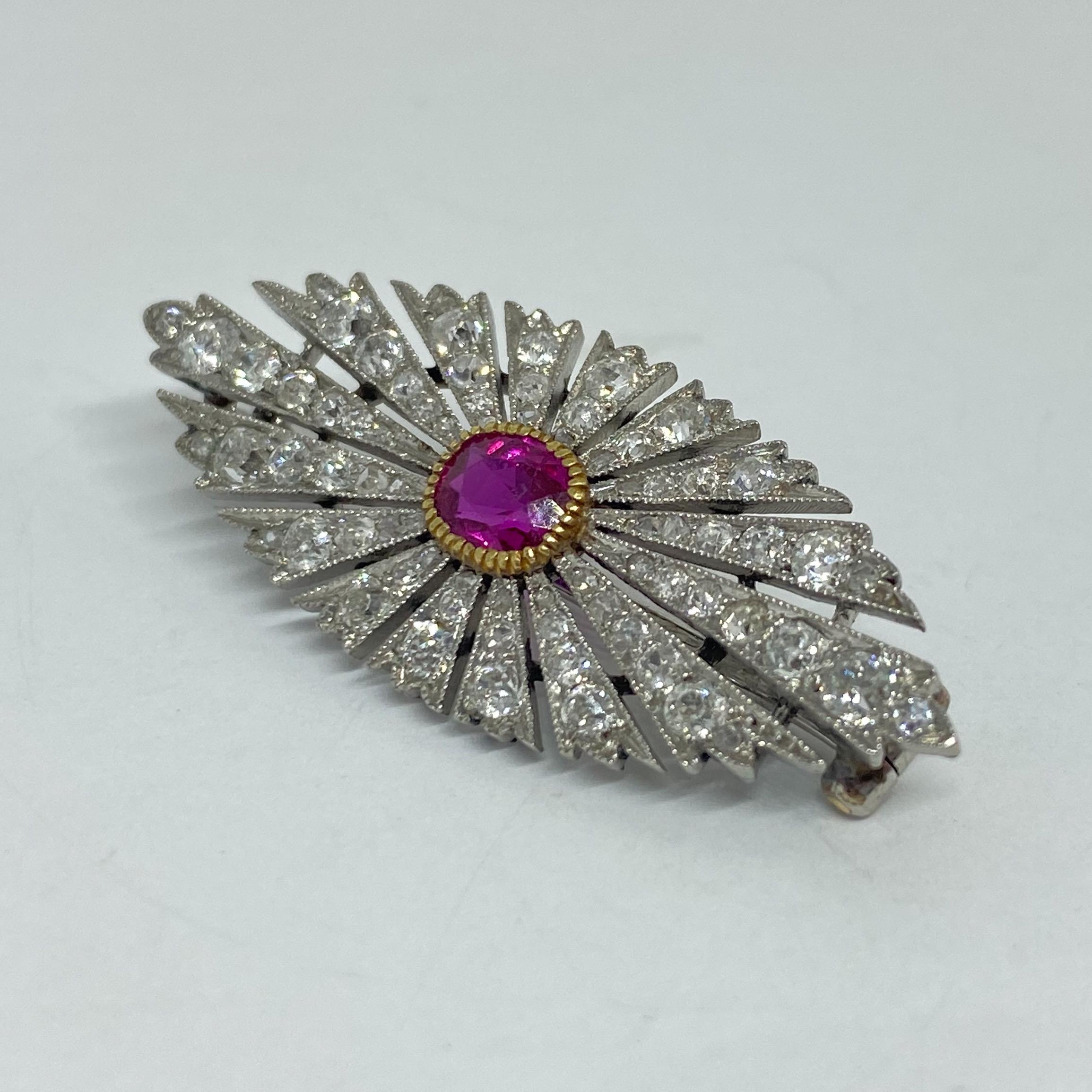 Antique Burma ruby and diamond brooch designed in platinum and 18K yellow gold. Diamonds are set in a marquise sun burst with milgrain and cutout rays. The center ruby is set in a yellow gold milgrain bezel. Hinged pin brooch with curled 