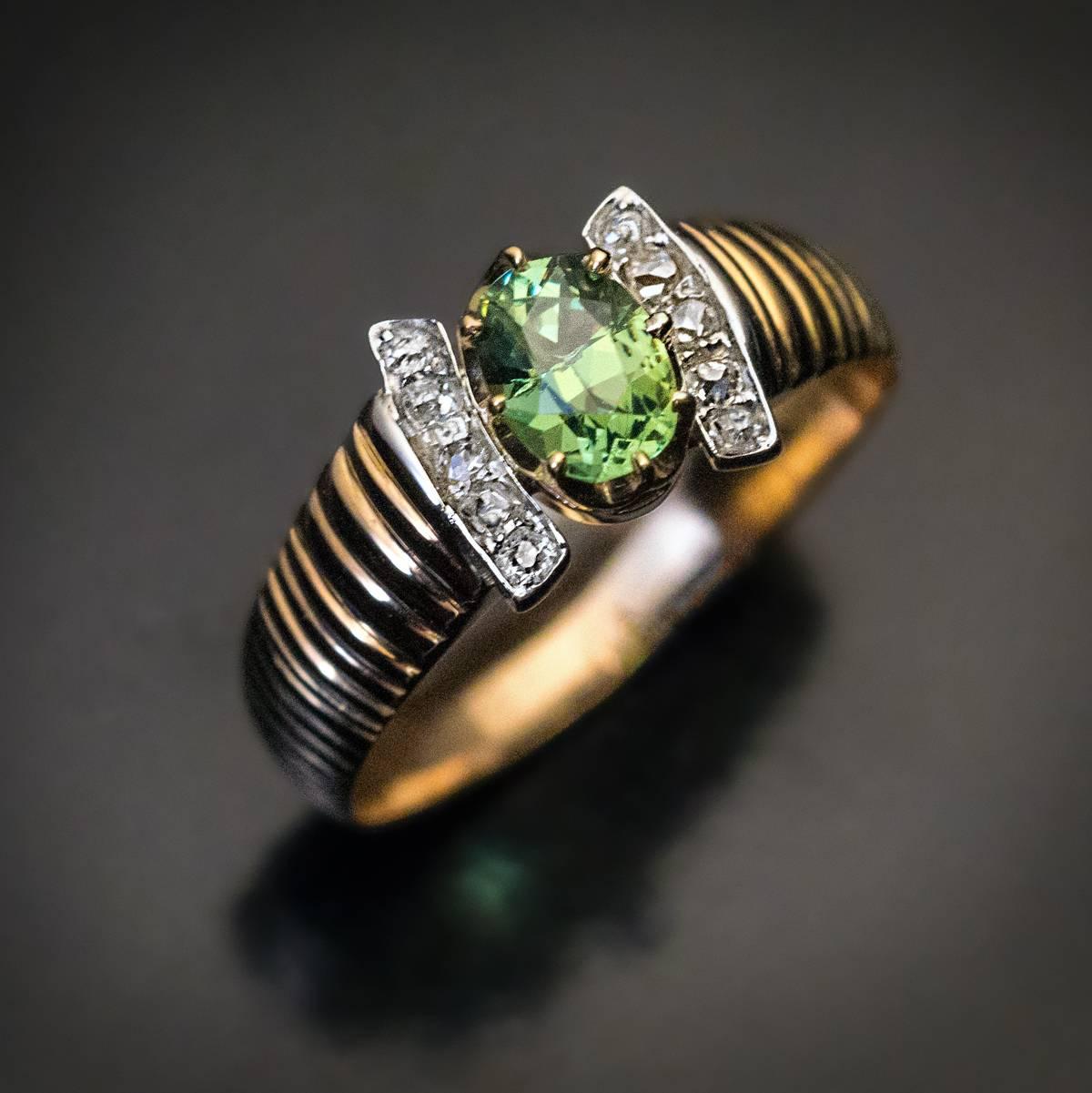 Circa 1890s

An antique ribbed gold ring is centered with a sparkling Russian demantoid garnet (measuring 6.05 x 4.6 x 3.2 mm, approximately 0.70 ct), flanked by two slightly curved silver bars set with old cut diamonds.

The ring is marked with 56