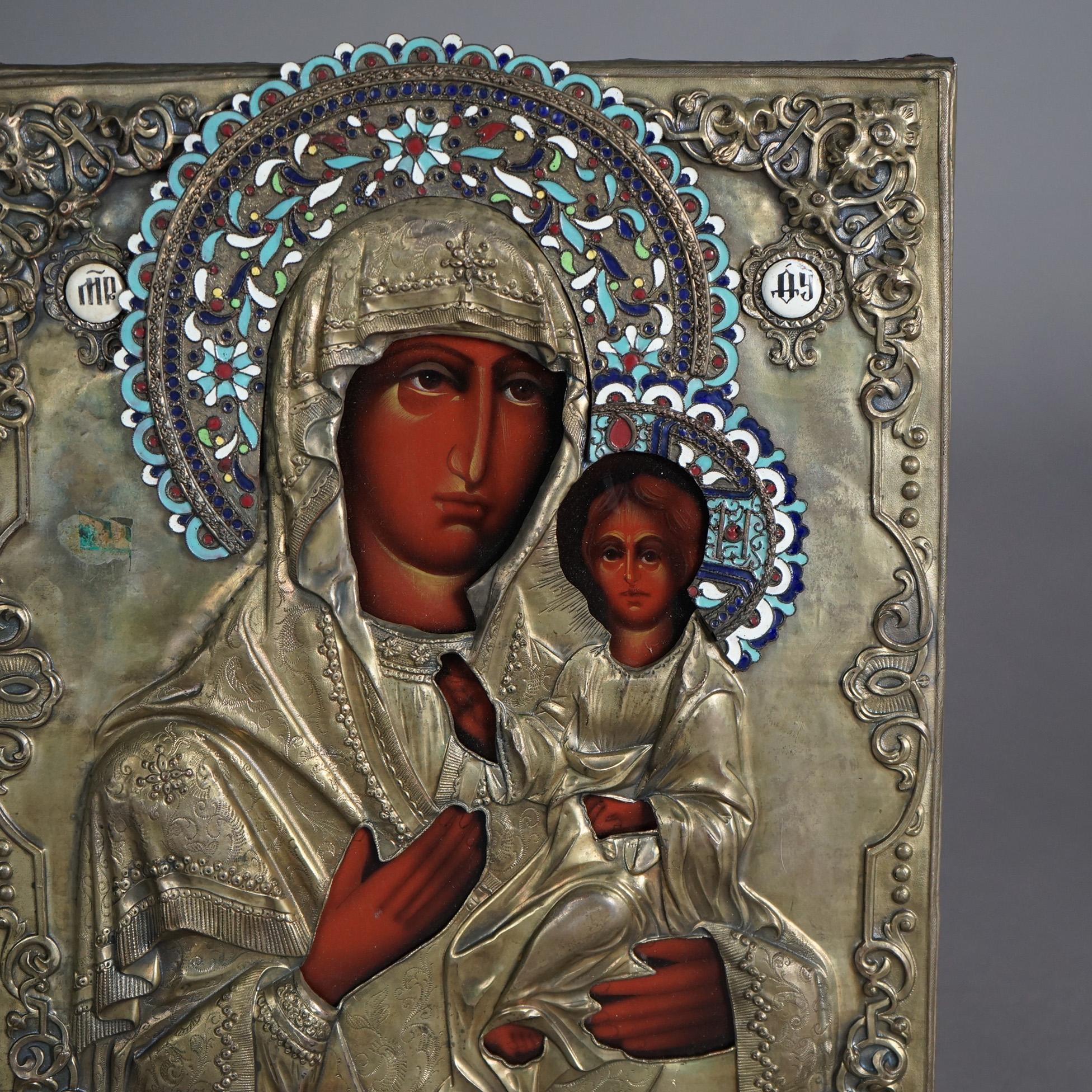 An antique Russian icon offers painted portrait on wood of Mother Mary and The Christ Child encased in embossed brass having enameled accepts, c1900

Measures - 12