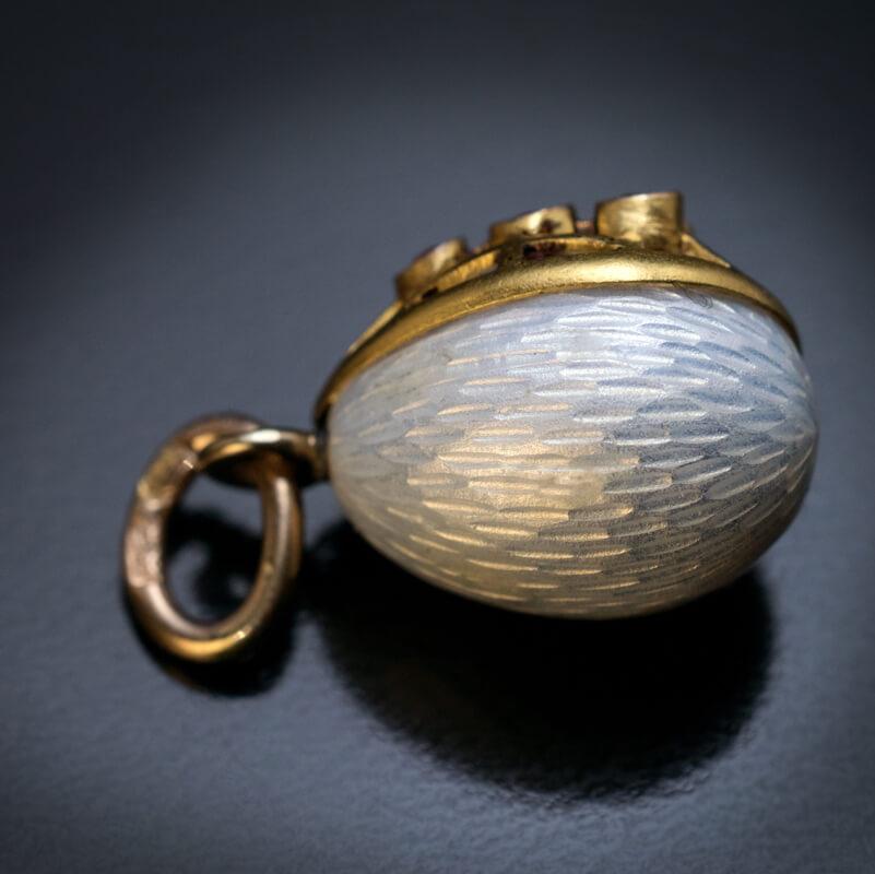 Made in St. Petersburg between 1908 and 1917 by W. Warburton.

This white guilloche enamel egg pendant with cage-like gold mount is embellished with nine faceted rubies. The design of the egg is clearly influenced by Faberge eggs of the same period.