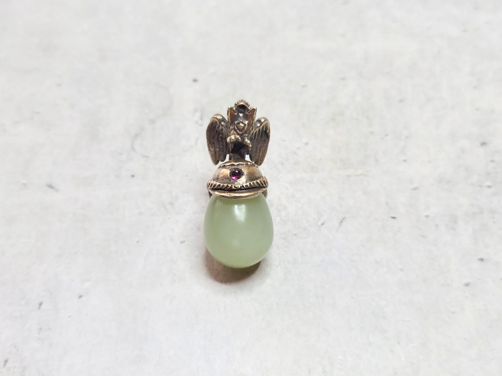 We present a beautiful egg pendant in the form of a miniature carved gilt silver helmet with a double-headed eagle and globus cruciger. It is truly a unique piece of jewelry, with a tiny garnet cabochon on the helmet and an egg-shaped bowenite