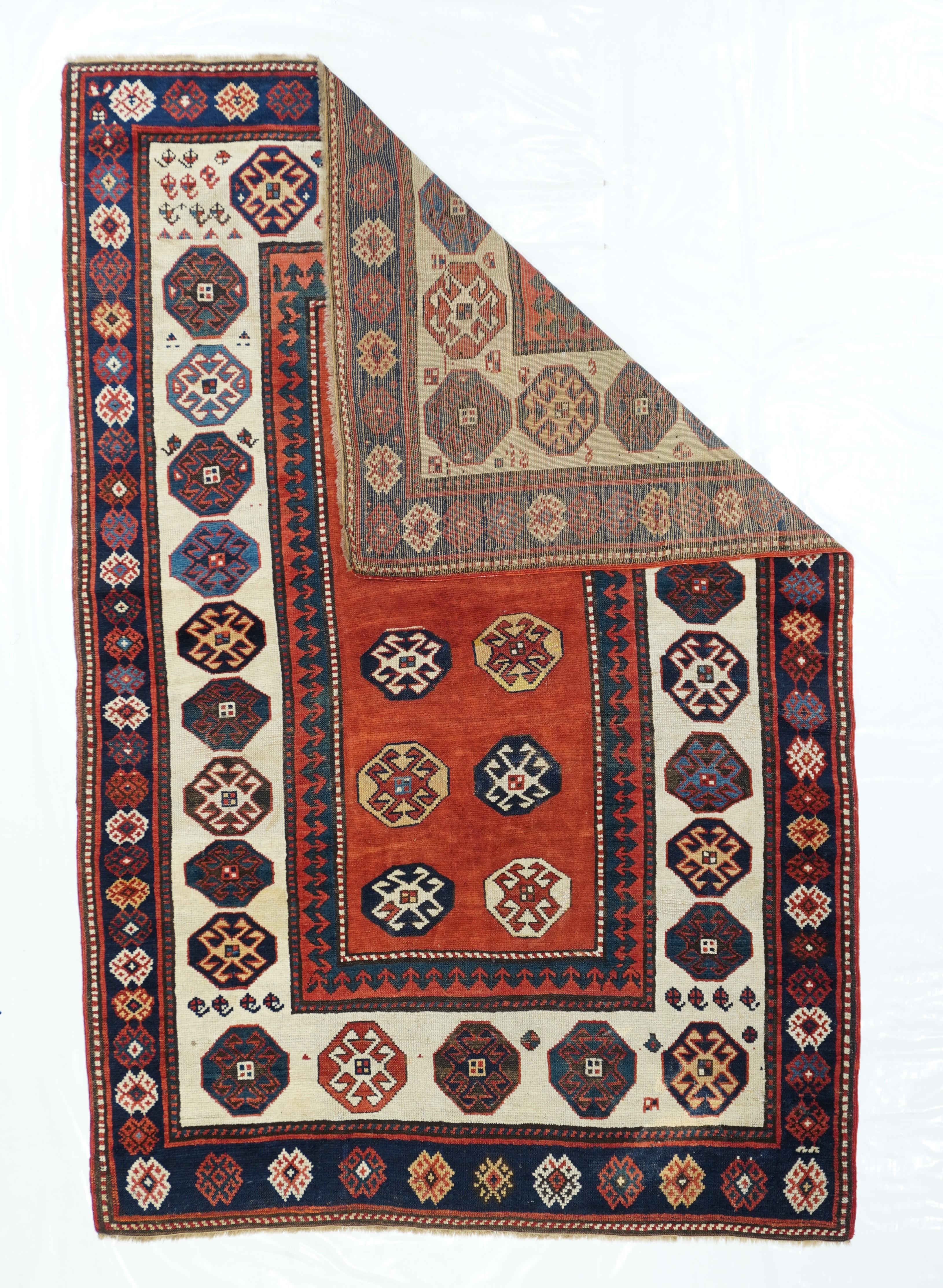 Tappeto Kazak antico 4'2'' x 6'4''. Questo sparpagliamento armeno di SW Caucasico, di grande semplicità, presenta un motivo uniforme di ottagoni che racchiudono diamanti uncinati sia nel campo rosso ruggine che nel bordo color guscio d'uovo. Il