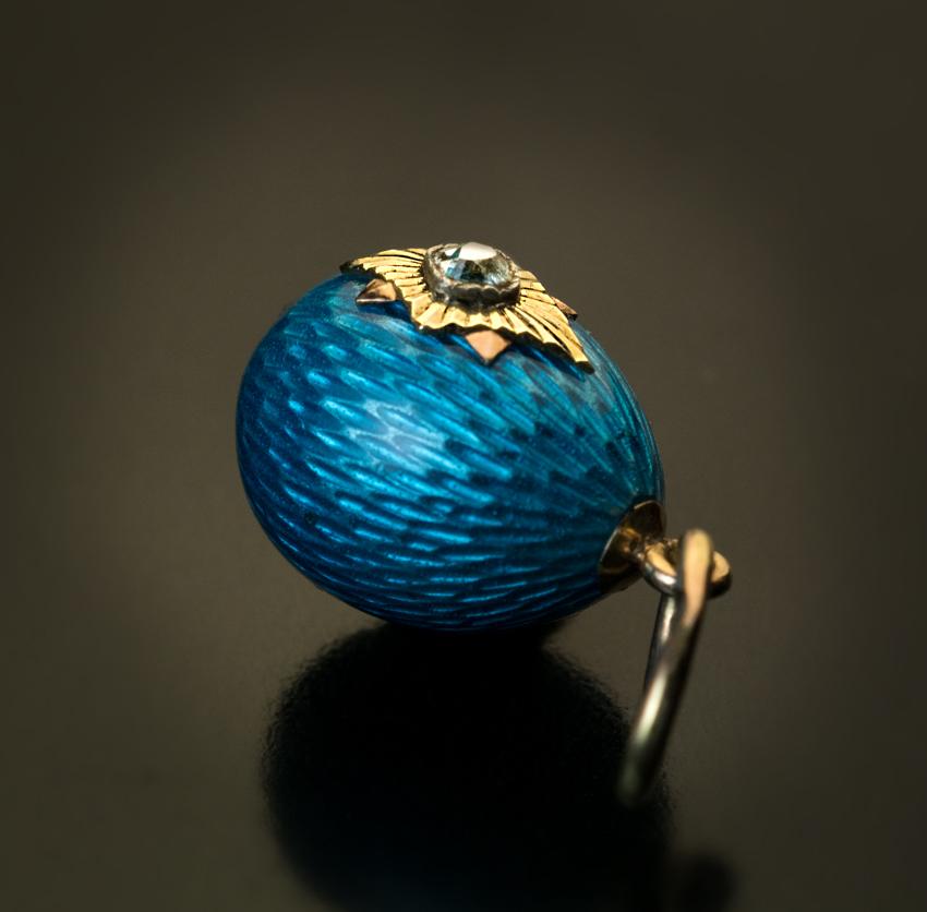 This antique Russian egg pendant was made between 1908 and 1917. The egg is covered with a brilliant turquoise blue guilloche enamel. One side of the egg is applied with a two-color gold star accented by an old mine cut diamond.
Marked with 56