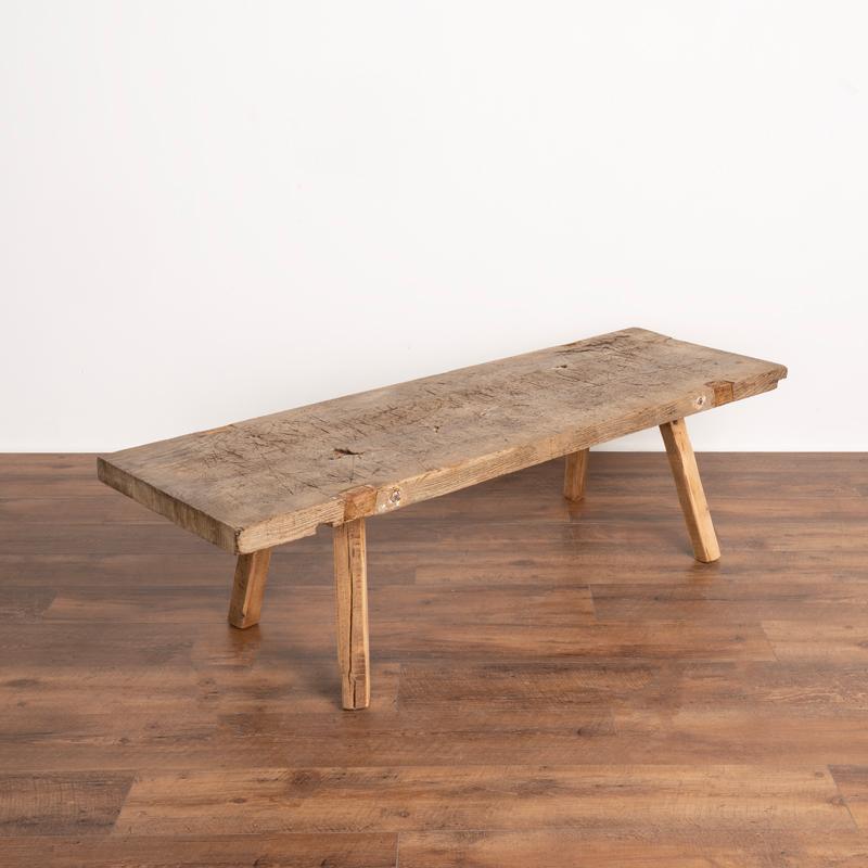 The thick slab top draws one to this rustic coffee table due to the heavy distress seen in every scratch, crack and deep gouge that came from years of constant use (likely in a butcher's shop). Note the old, contrasting repairs of wood seen in the
