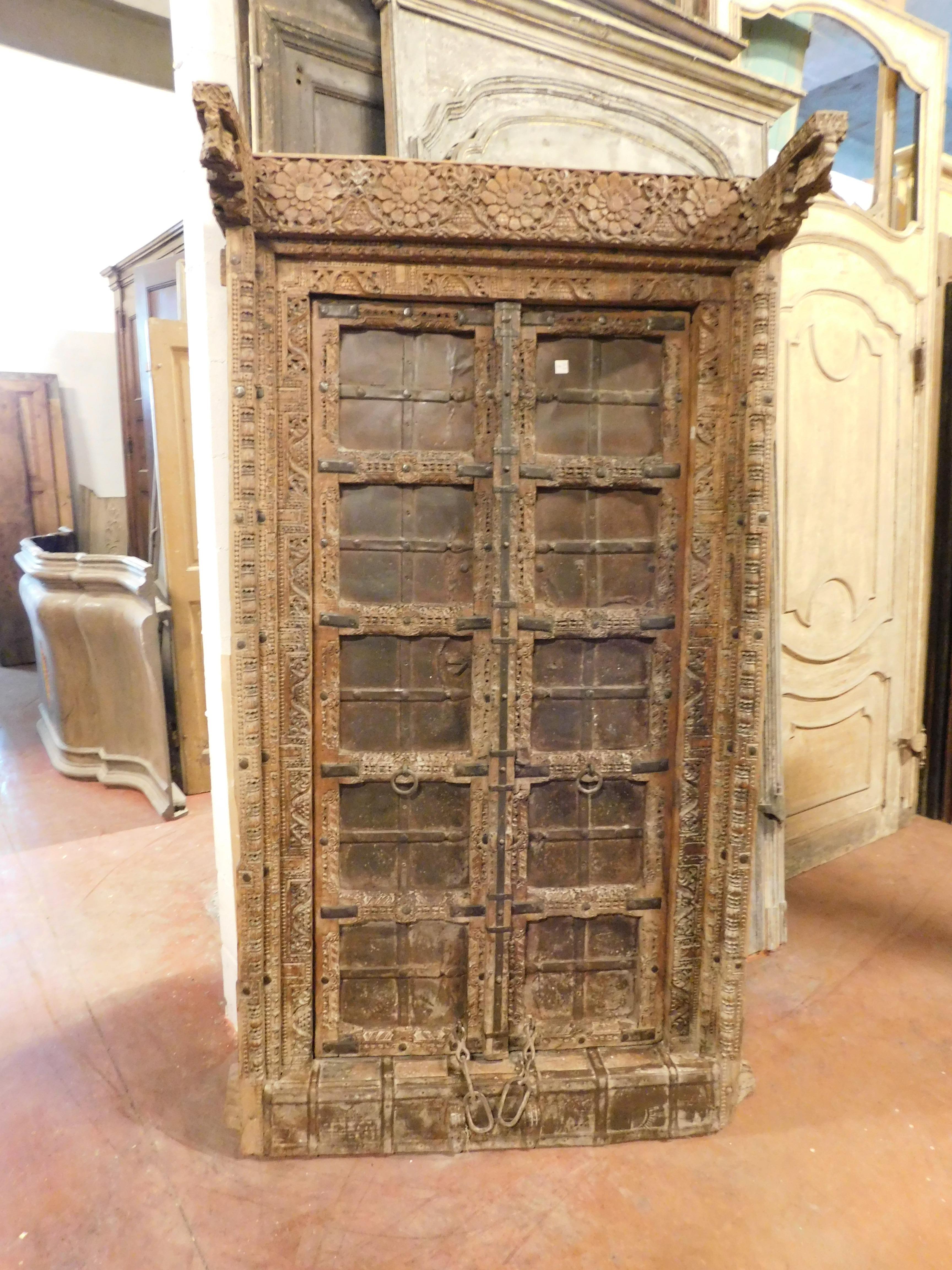 Antique rustic ethnic entrance door, strong and robust carved brown wood, complete with frame and original irons, chains and coverings. They were well designed to withstand inclement weather and theft, very massive, they have an iron strip cover and