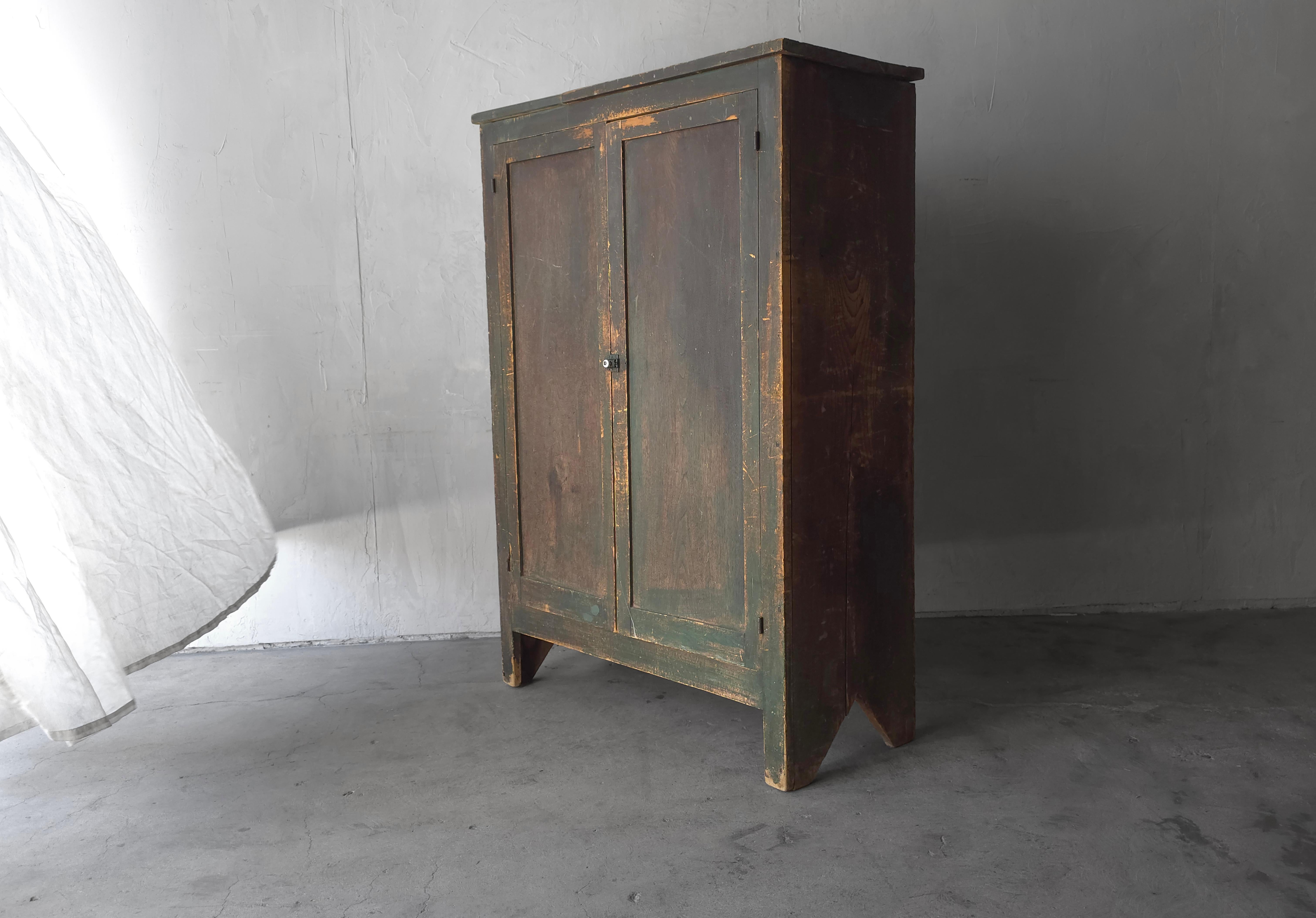 This antique cabinet exudes a kind of charm and timeworn character that can only come from centuries of use.   Crafted from solid wood, its surface bears the marks of age—weathered textures, worn edges, and faded traces of original green paint that