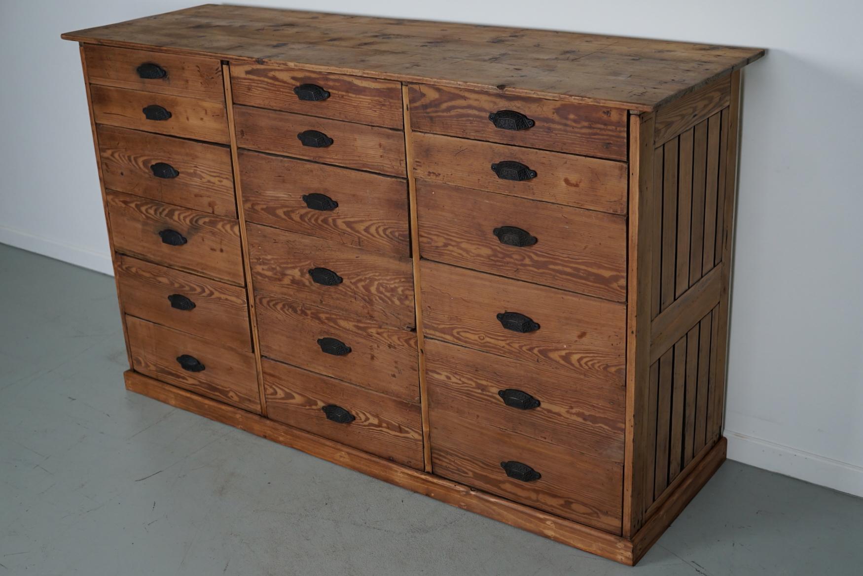 This apothecary bank of drawers was designed and made circa 1900. It was made from pine and it features 18 drawers with cast iron handles. The interior dimensions of the drawers are: DWH 40 x 42 x 8 / 15 cm.