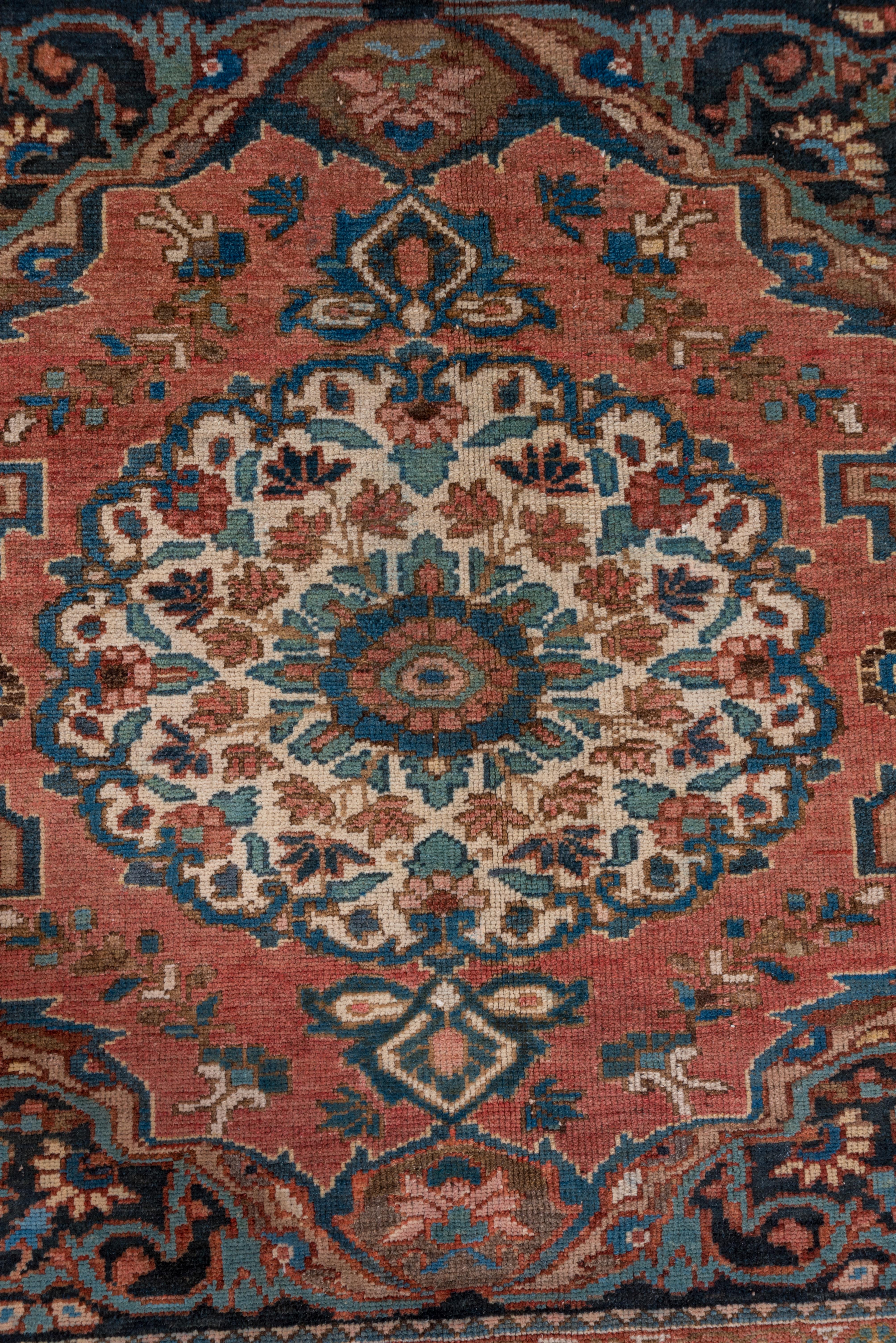 The navy field of this rustic central Persian Chahar Mahal rug is almost completely covered by four light red conjoined cartouches, each enclosing an ivory pendanted floral roundel with piecrust edges.Light blue tendrils fill in around the major