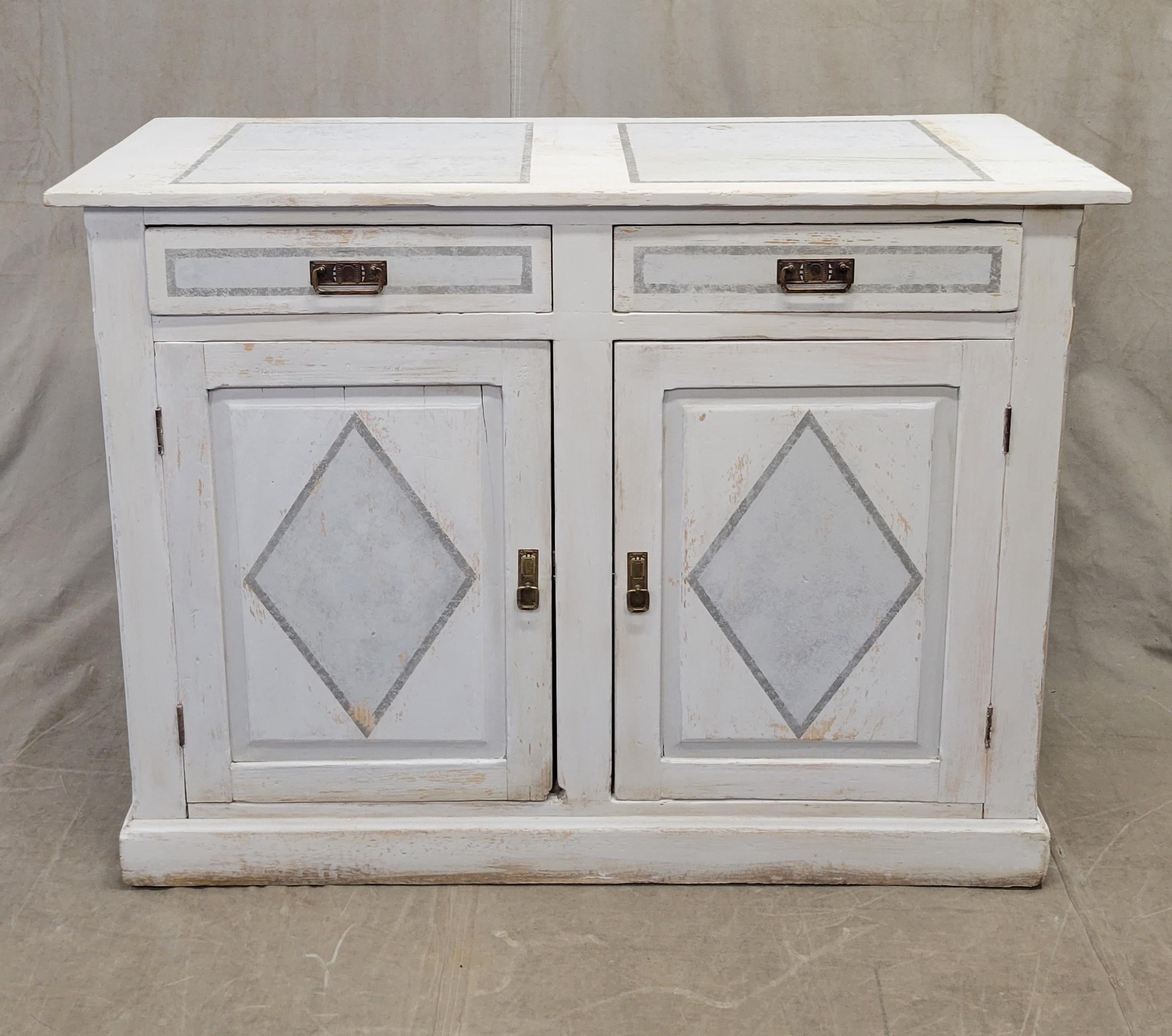 This charming antique pine farmhouse cabinet is white washed and accented with gray decorative paint and brass hardware. It is a rustic but strong and stable piece that offers a good amount of storage. Note the wood separation in the top from