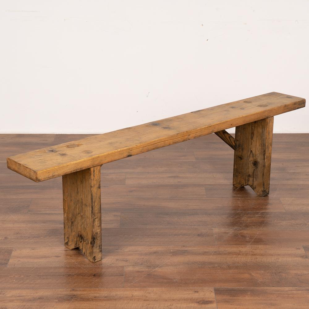 Rustic plank top bench with deep aged patina.
The top reveals generations of use with nicks, stains and scuffs which add character to the narrow bench.
Restored and waxed, this bench is strong, stable and ready for use. 
Any scratches, cracks,