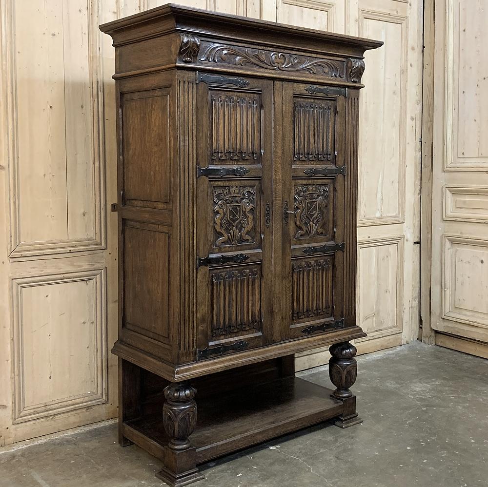 Antique rustic Renaissance raised Bonnetiere combines linenfold panels with family crest carvings, creating doors that are mounted with forged iron strap hinges. Urn pediments support the casework above and flank a lower display shelf. Finely carved