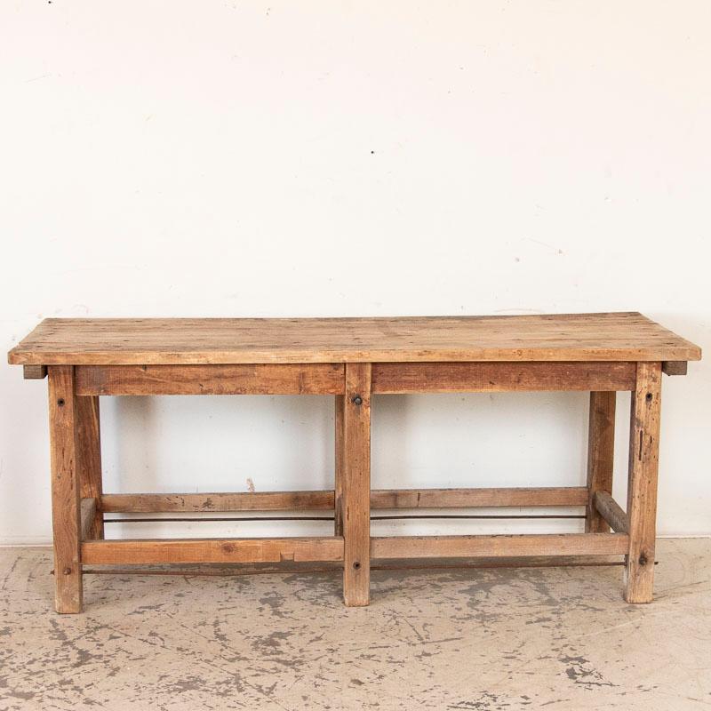 The appeal of this work table comes from the worn, weathered look created from the generations of use it has received. Notice the metal rods, now rusted with age, which create added support to the four stretchers. The plank top shows expected
